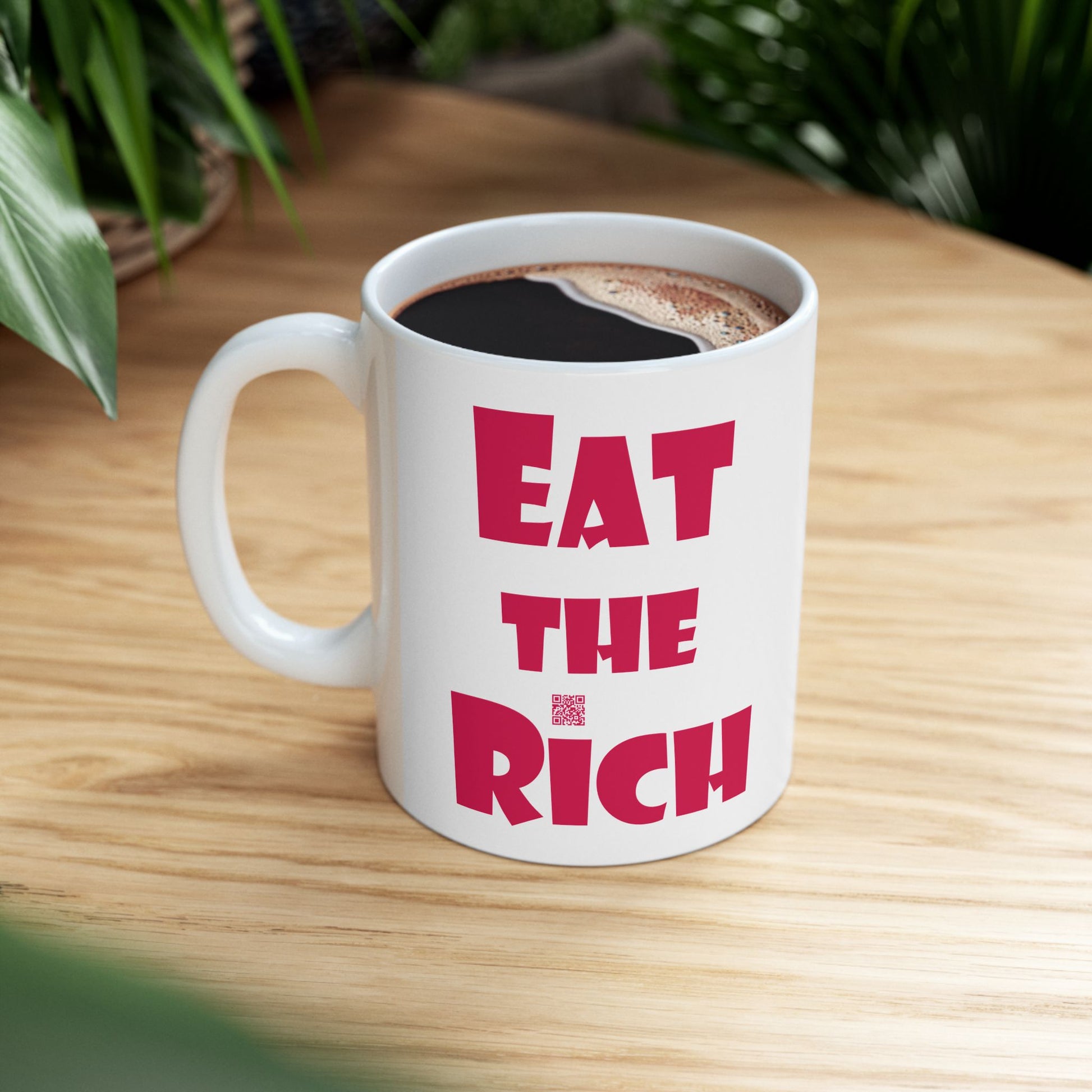 White EAT THE RICH 11oz Ceramic Mug featuring bold red text on a wooden table.