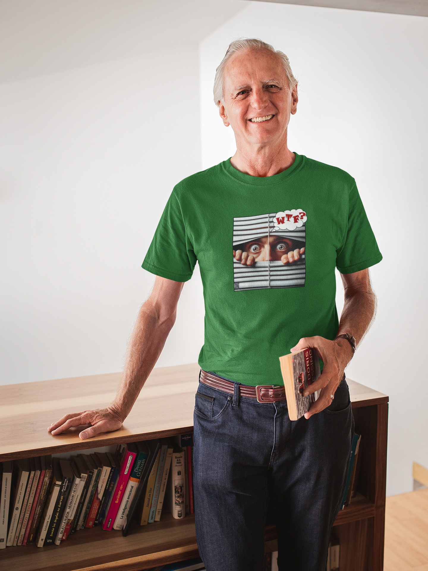 A senior man wearing a green WTF White Male Model Activist Tshirt, standing beside a bookshelf, smiling with a book in hand.
