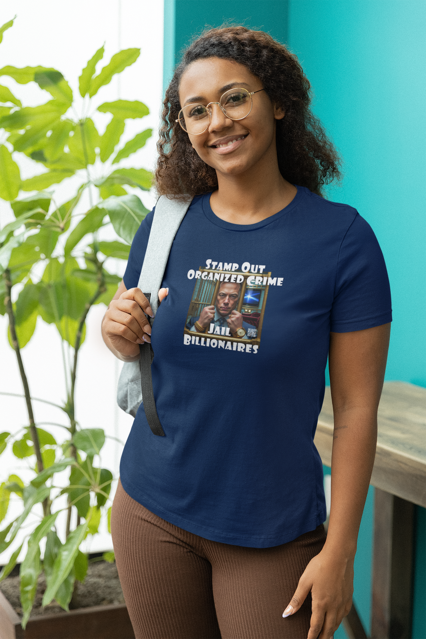 Woman wearing Stamp Out Organized Crime-Jail Billionaires Activist T-shirt in front of a plant.