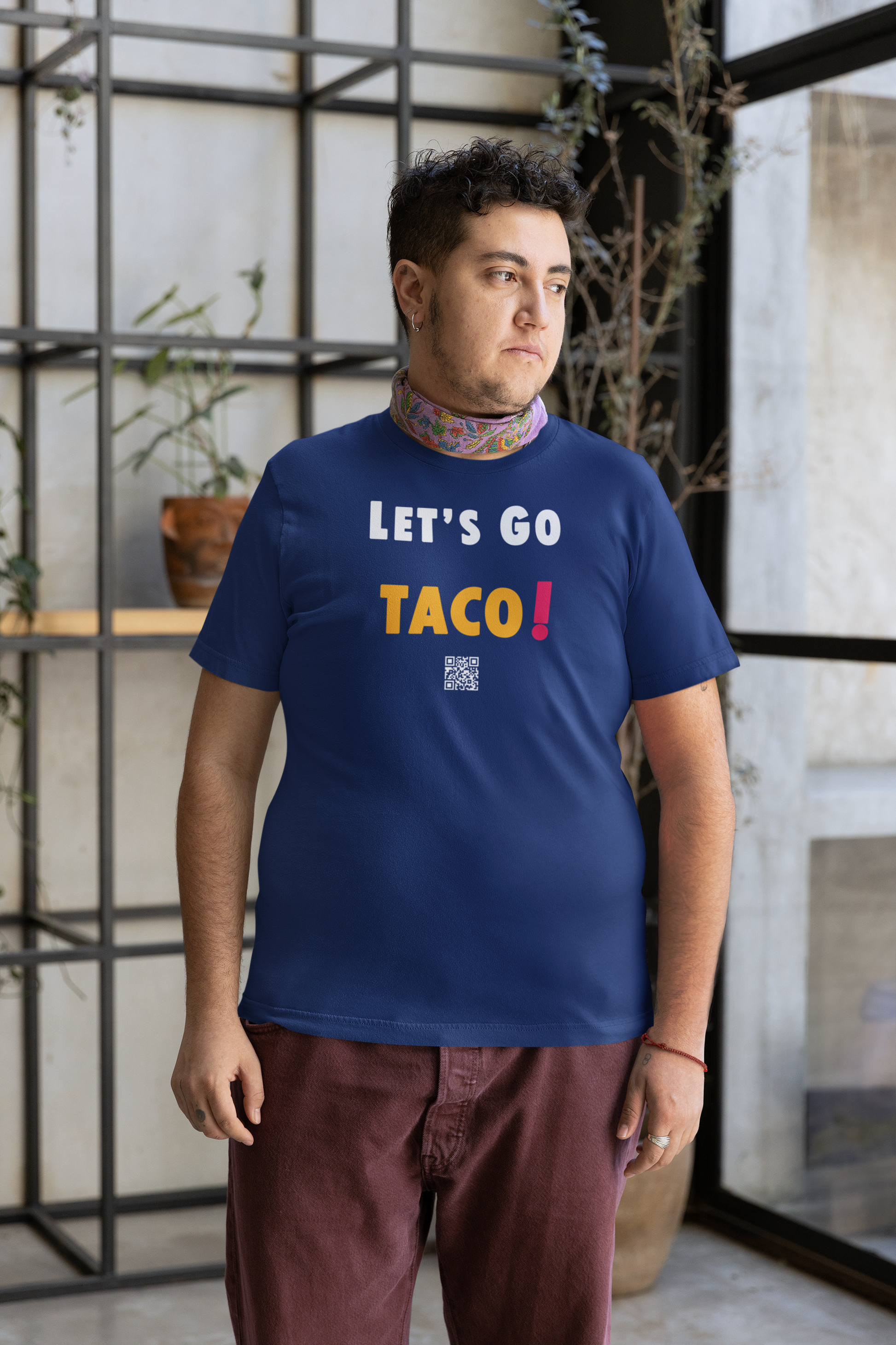 Model wearing a blue TACO Activist TShirt with text 'LET'S GO TACO!' in a modern indoor setting.