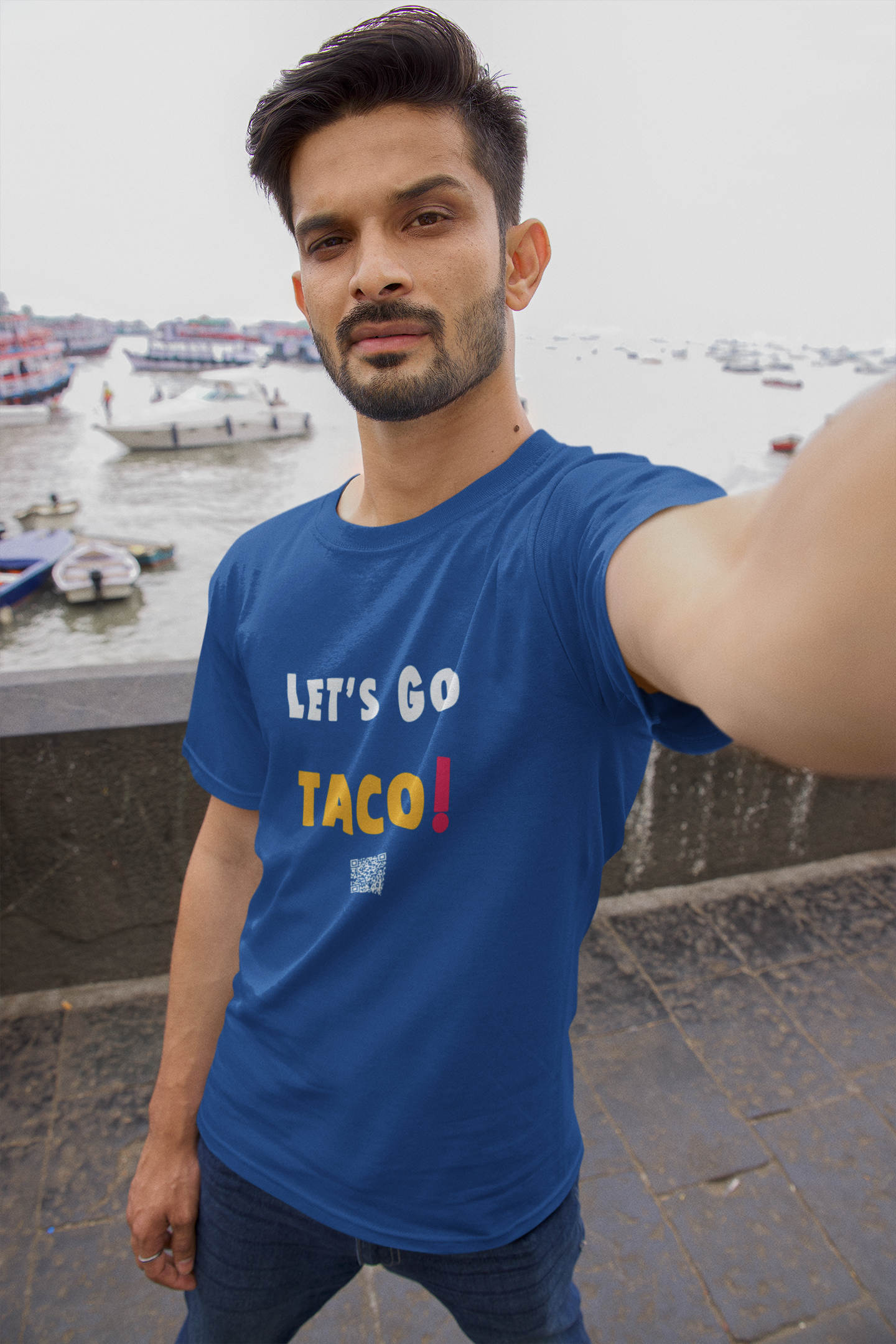 A man wearing a blue TACO Activist TShirt that says 'LET'S GO TACO!' with boats in the background.