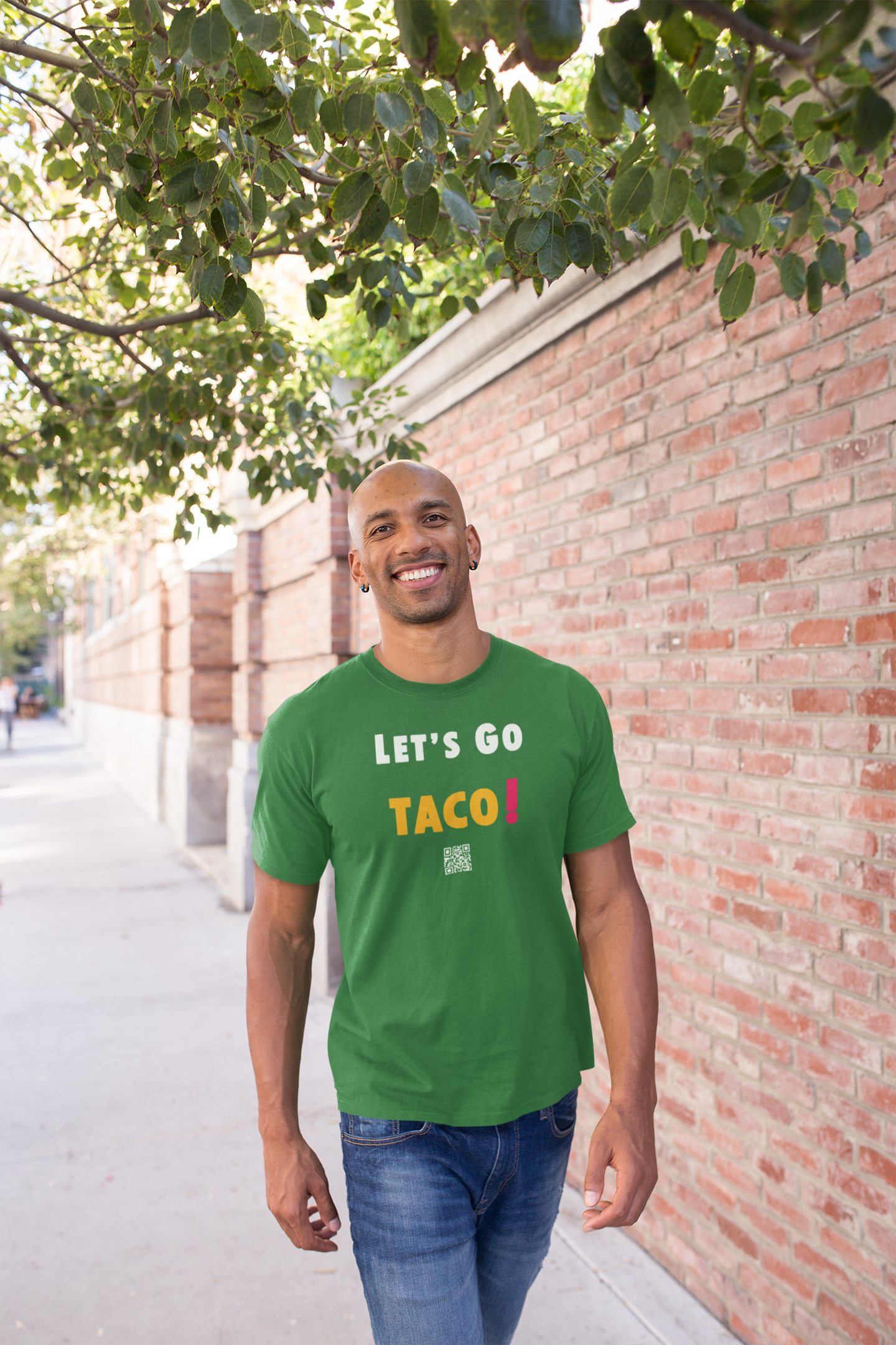 Man wearing a green TACO Activist TShirt with the text 'LET'S GO TACO!' walking on a city street.
