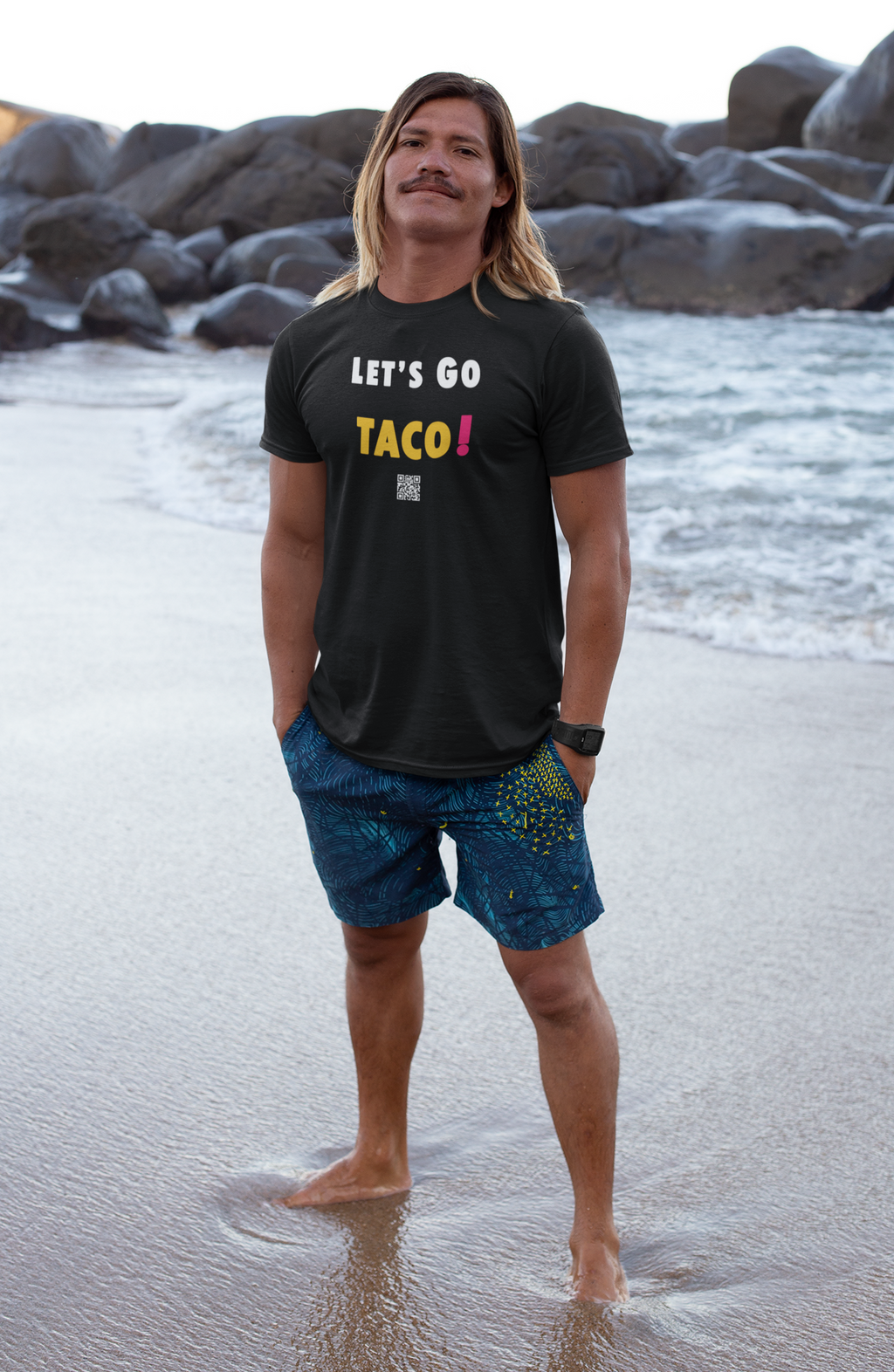 Adult male wearing TACO Activist TShirt at the beach with ocean waves in the background.
