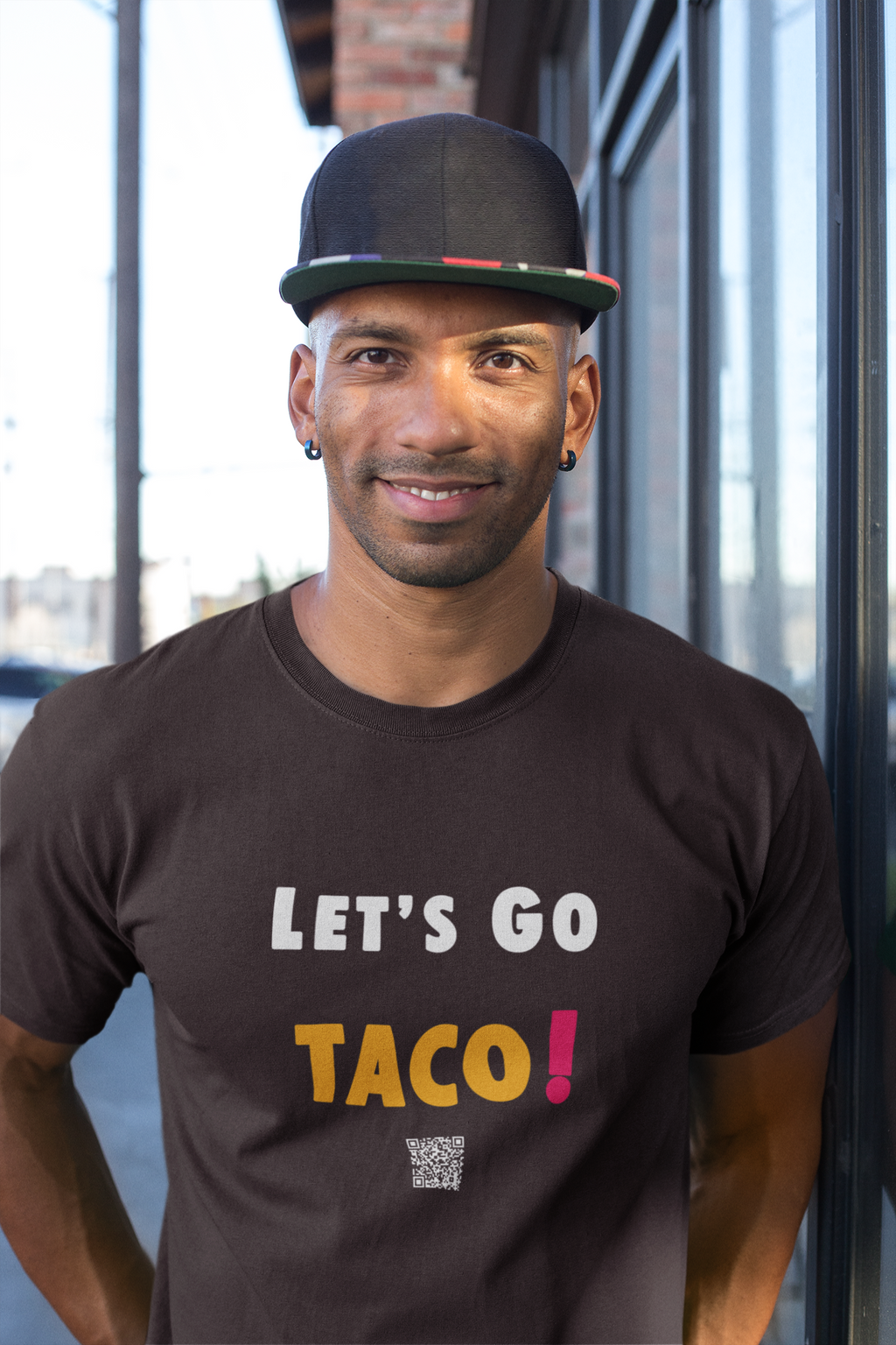 Man wearing a TACO Activist TShirt with the text 'LET'S GO TACO!' in a casual urban setting.