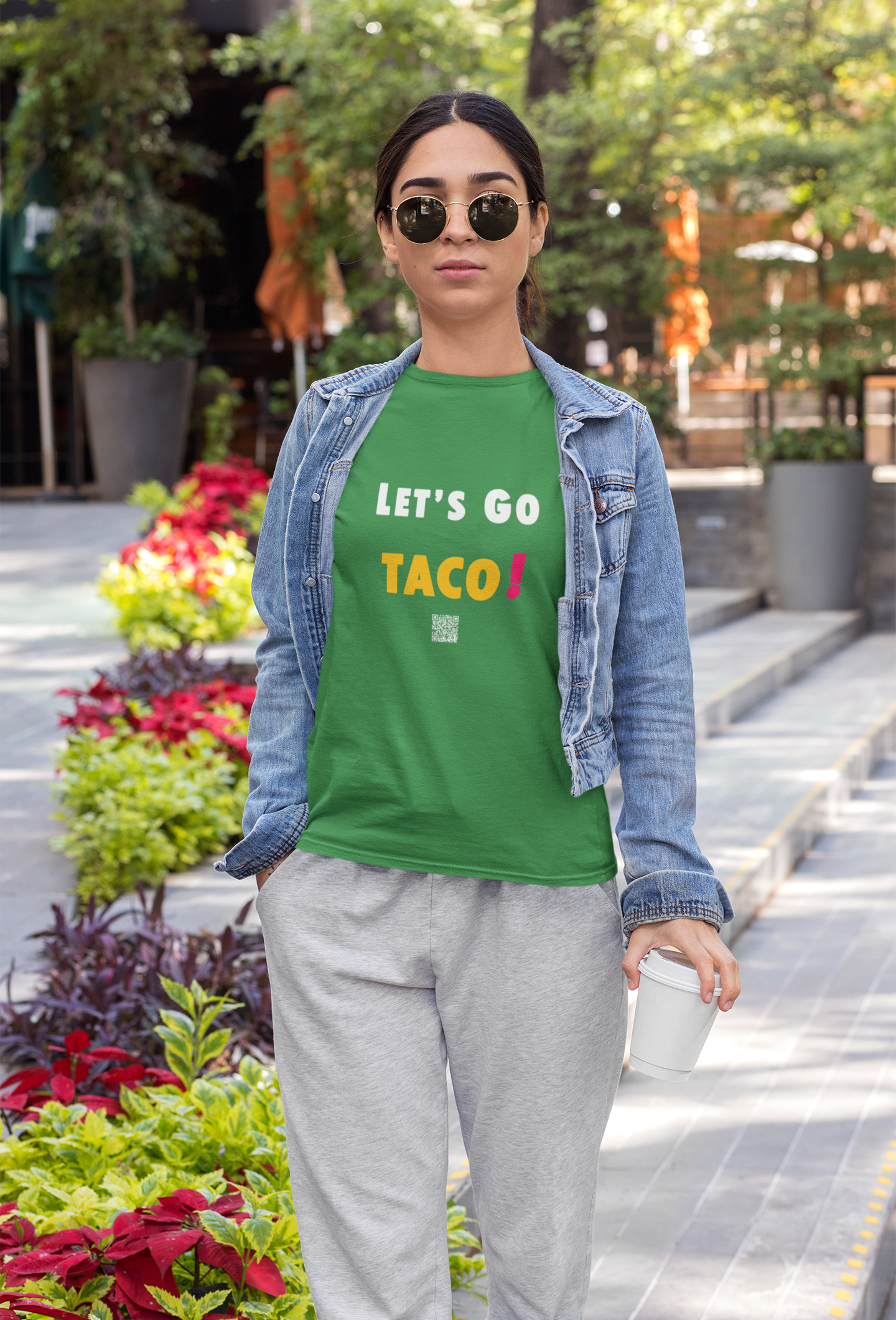 A woman wearing a green TACO Activist TShirt with sunglasses in a lively outdoor setting.