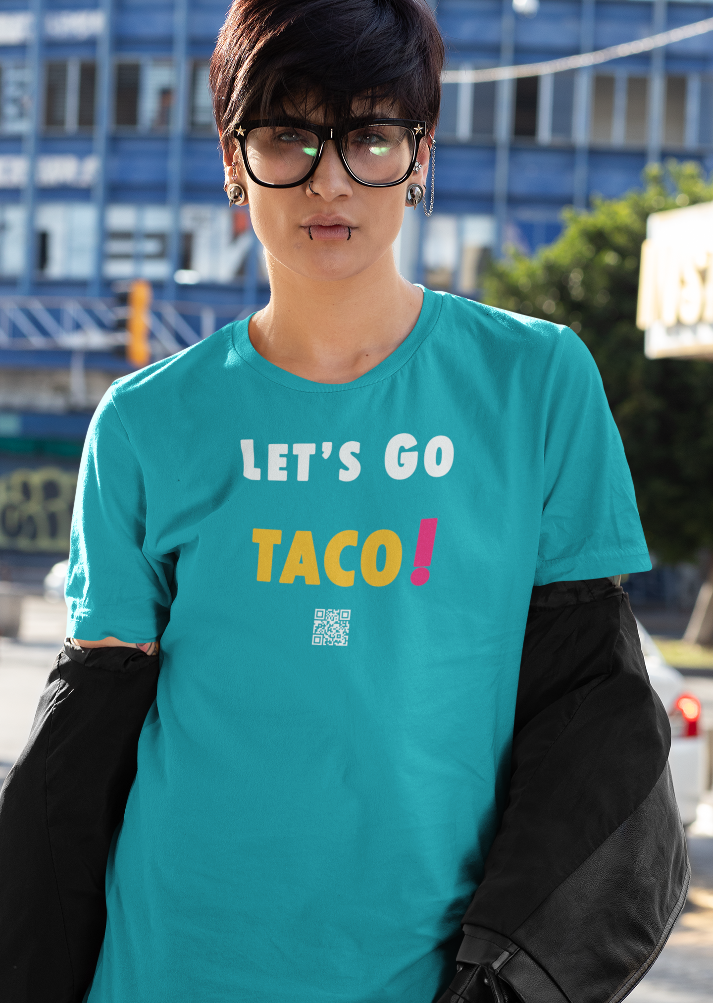 Model wearing a TACO Activist TShirt in turquoise, featuring the phrase 'LET'S GO TACO!' in colorful letters.