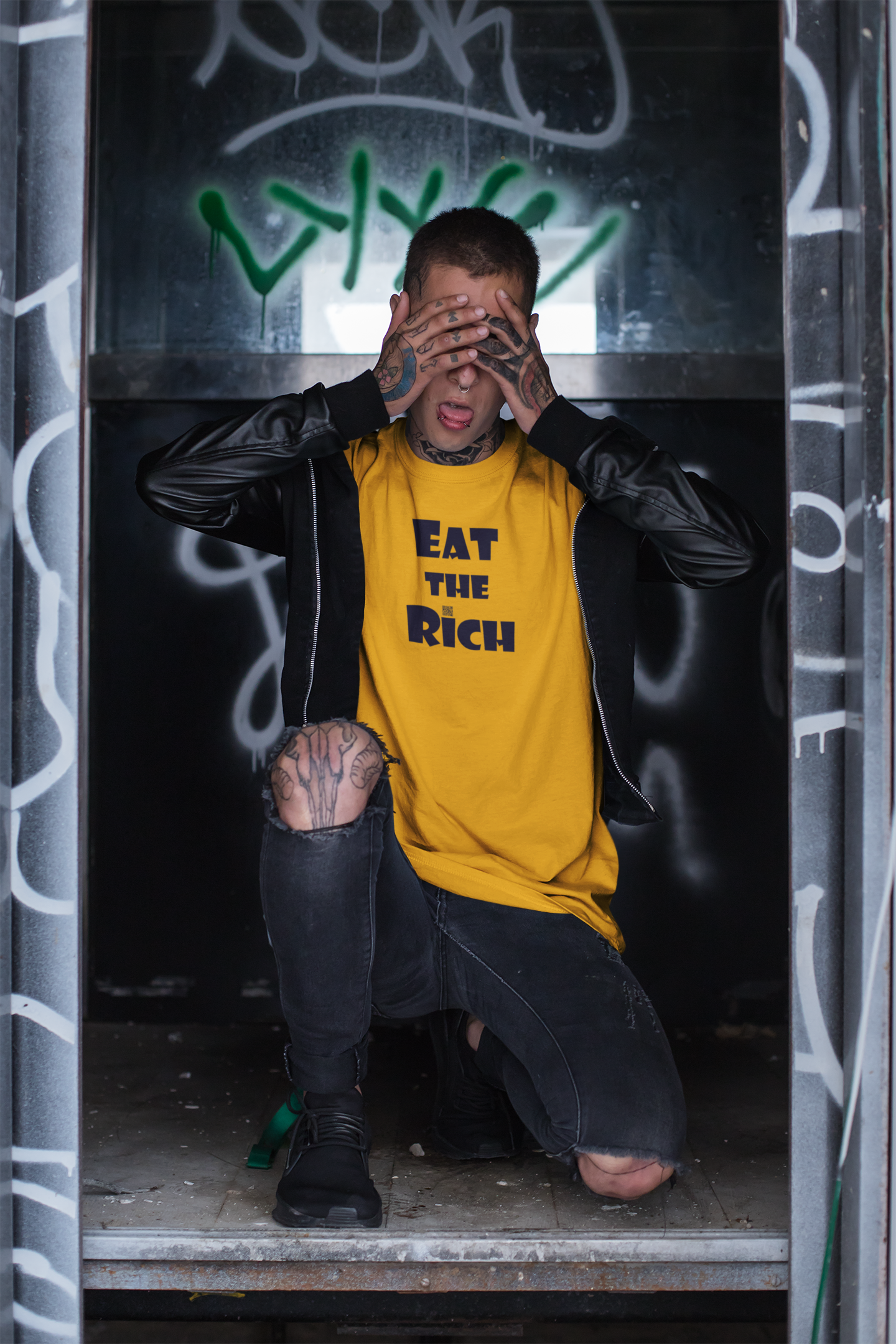 Person wearing EAT THE RICH Unisex TShirt in bold font, crouching in a graffiti-filled environment.