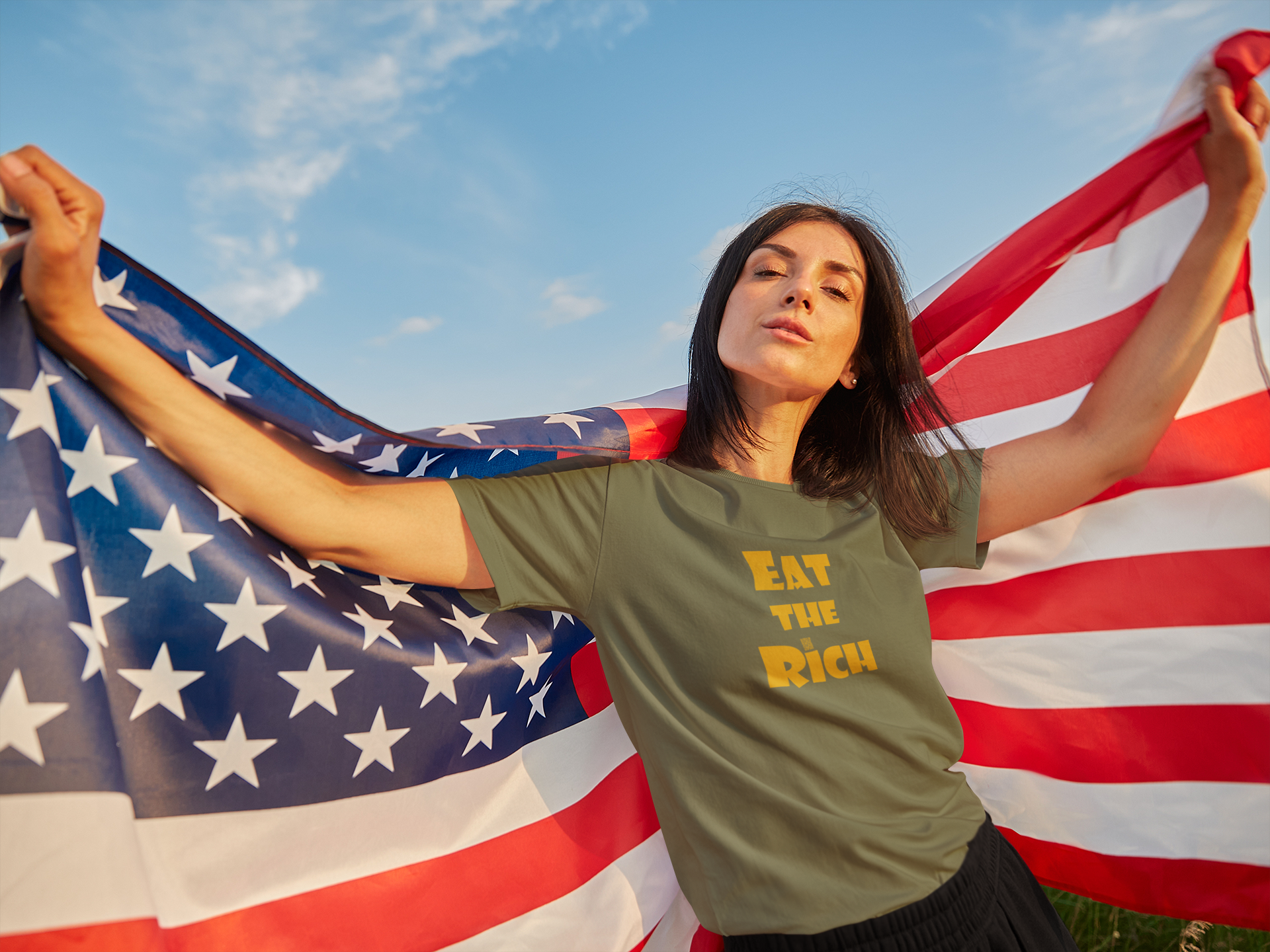 Model wearing EAT THE RICH Unisex TShirt, holding American flag, showcasing bold protest statement.