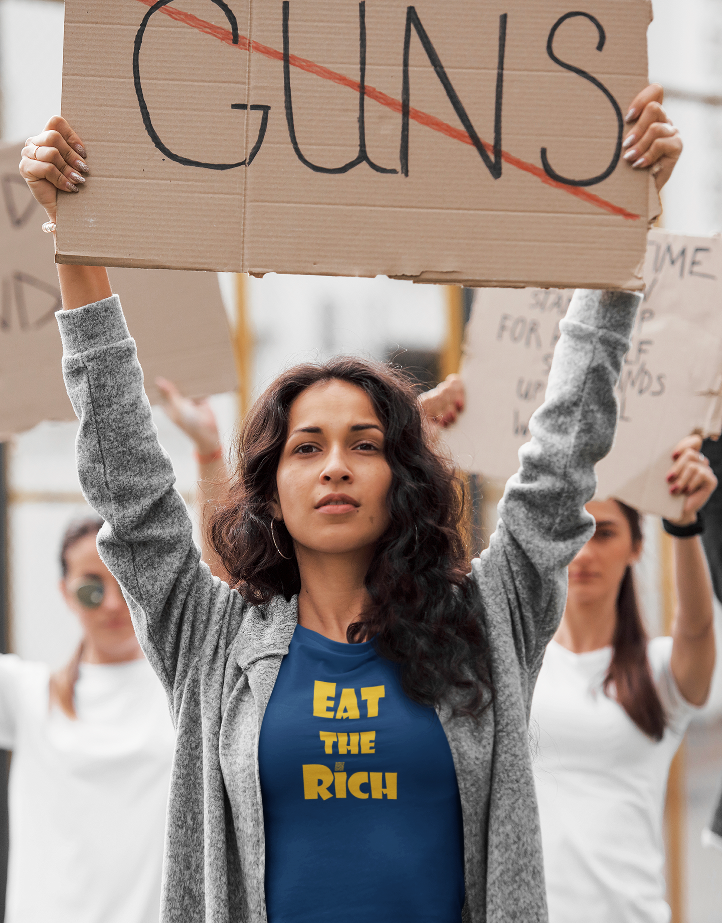 Woman wearing EAT THE RICH Unisex TShirt at a protest, holding a sign against guns.