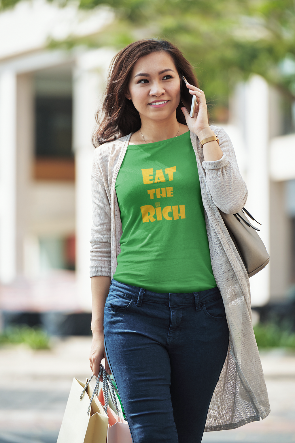 A woman wearing an EAT THE RICH Unisex TShirt while shopping outdoors, showcasing bold lettering on a green shirt.