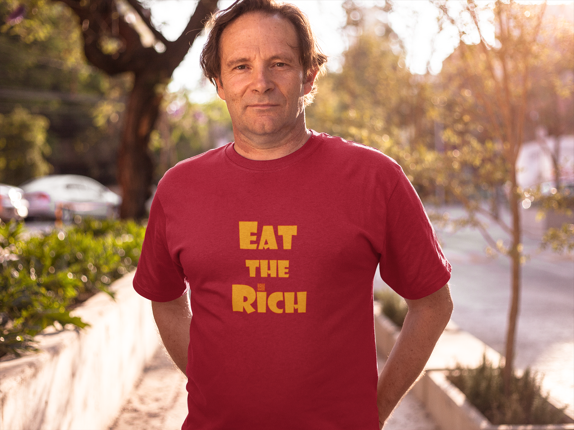 EAT THE RICH Unisex TShirt worn by a man outdoors, showcasing bold yellow text on a red shirt.