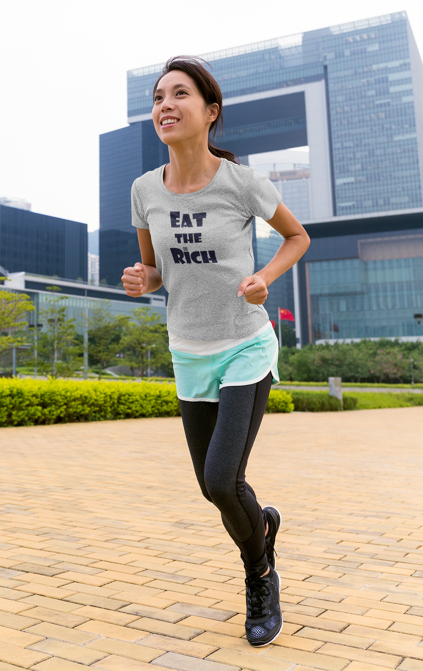 Woman jogging outdoors wearing an EAT THE RICH Unisex TShirt with a city skyline in the background.