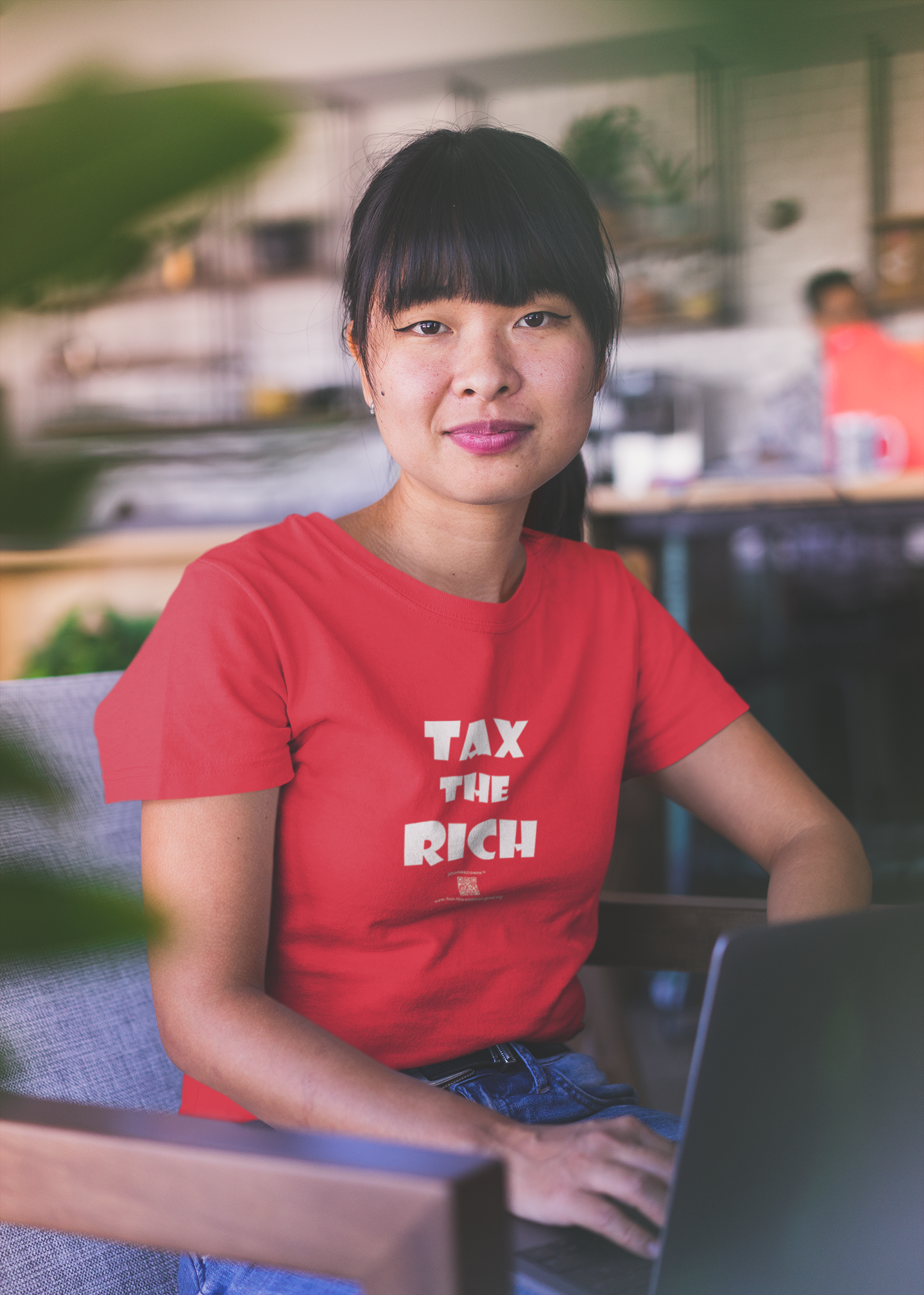 Model wearing a red TAX THE RICH Unisex T-Shirt, showcasing bold design in a modern workspace.