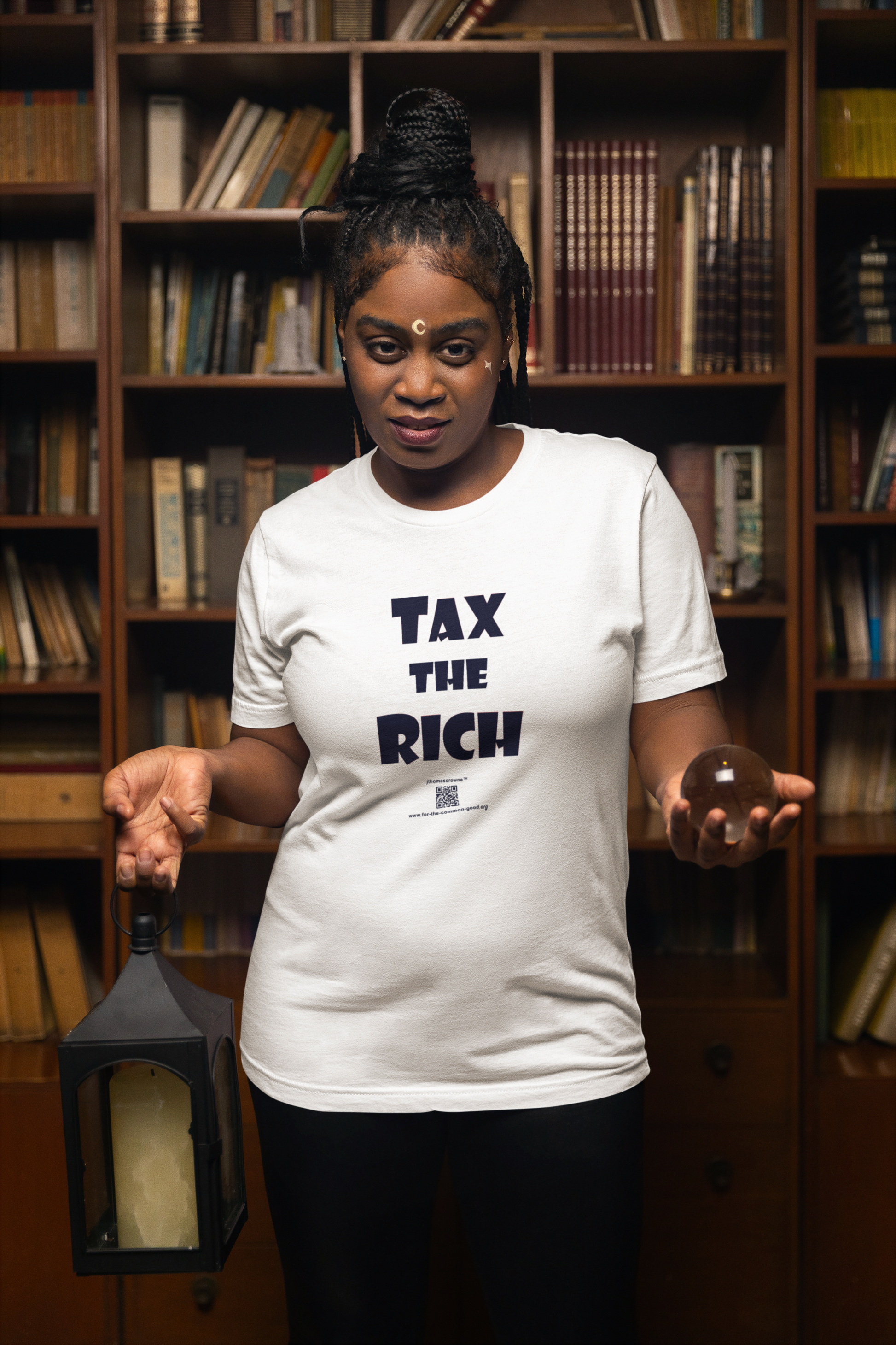 Model wearing a TAX THE RICH Unisex T-Shirt, holding a lantern, surrounded by books in a cozy library setting.