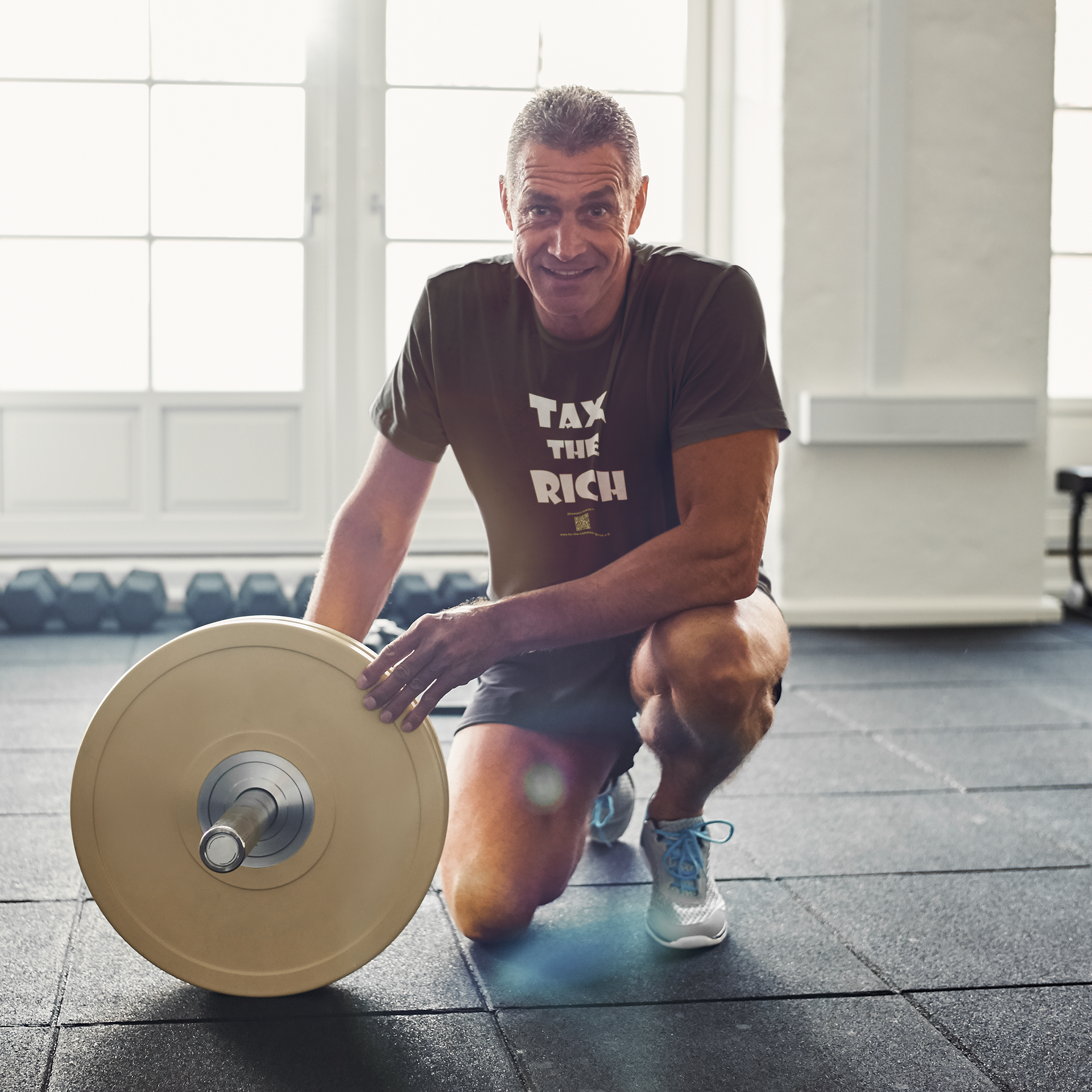 Man in gym wearing TAX THE RICH Unisex T-Shirt, kneeling with a barbell, representing wealth awareness.