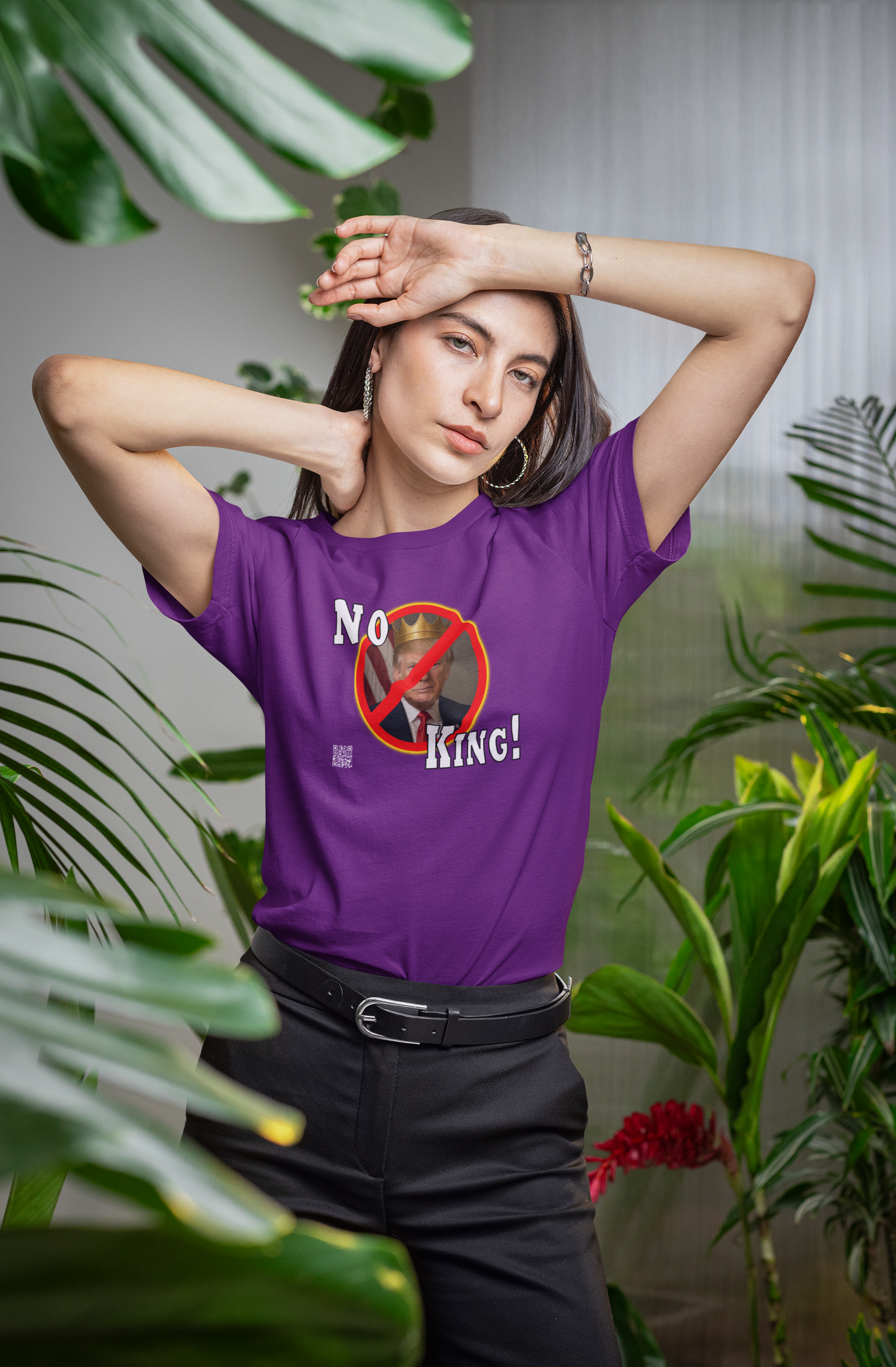 Woman wearing No King Activist TShirt in a vibrant purple color surrounded by indoor plants.