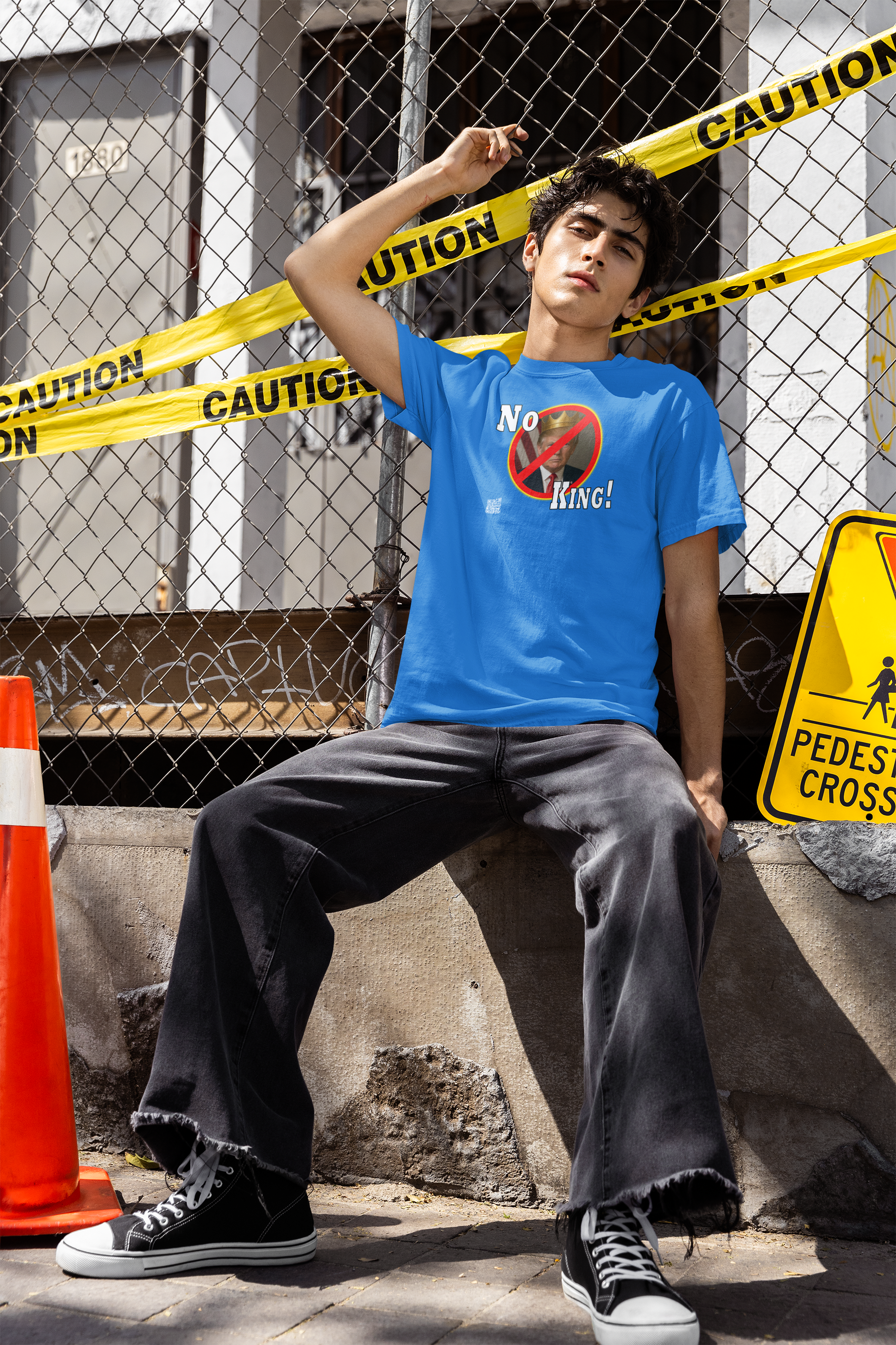 Model wearing No King Activist TShirt in front of a caution tape backdrop with traffic cones.