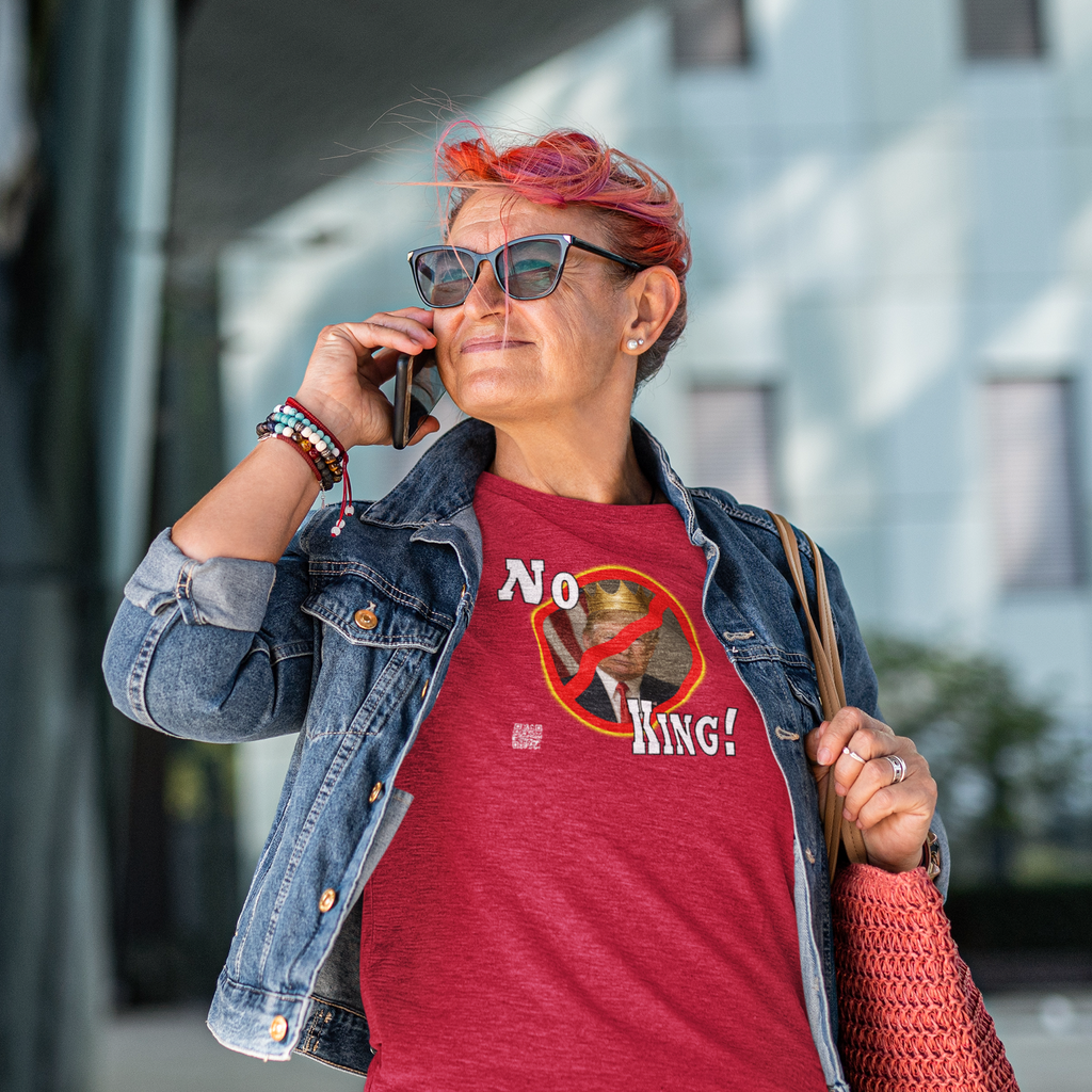 Woman wearing a No King Activist TShirt and denim jacket, confidently talking on the phone outdoors.