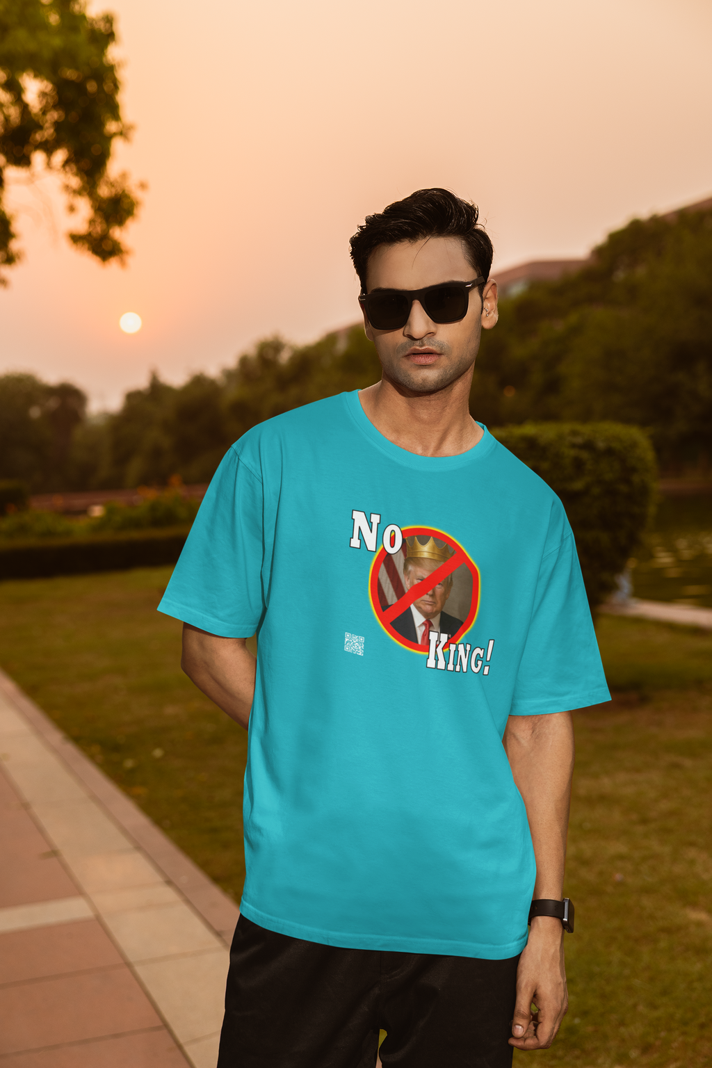 Model wearing No King Activist TShirt in turquoise, showcasing the bold design against a sunset background.