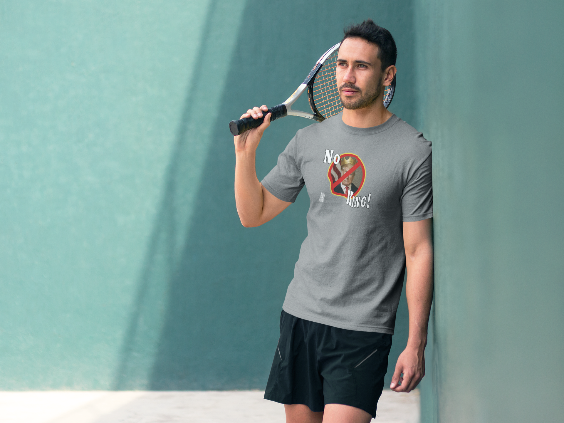 Man wearing No King Activist TShirt while holding a tennis racket against a green wall.