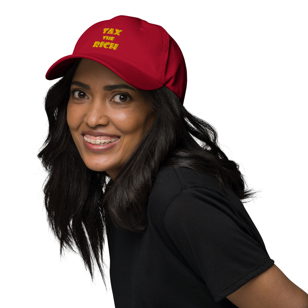 Person wearing a red hat with bold text saying TAX THE RICH — Embroidered Dad Hat.