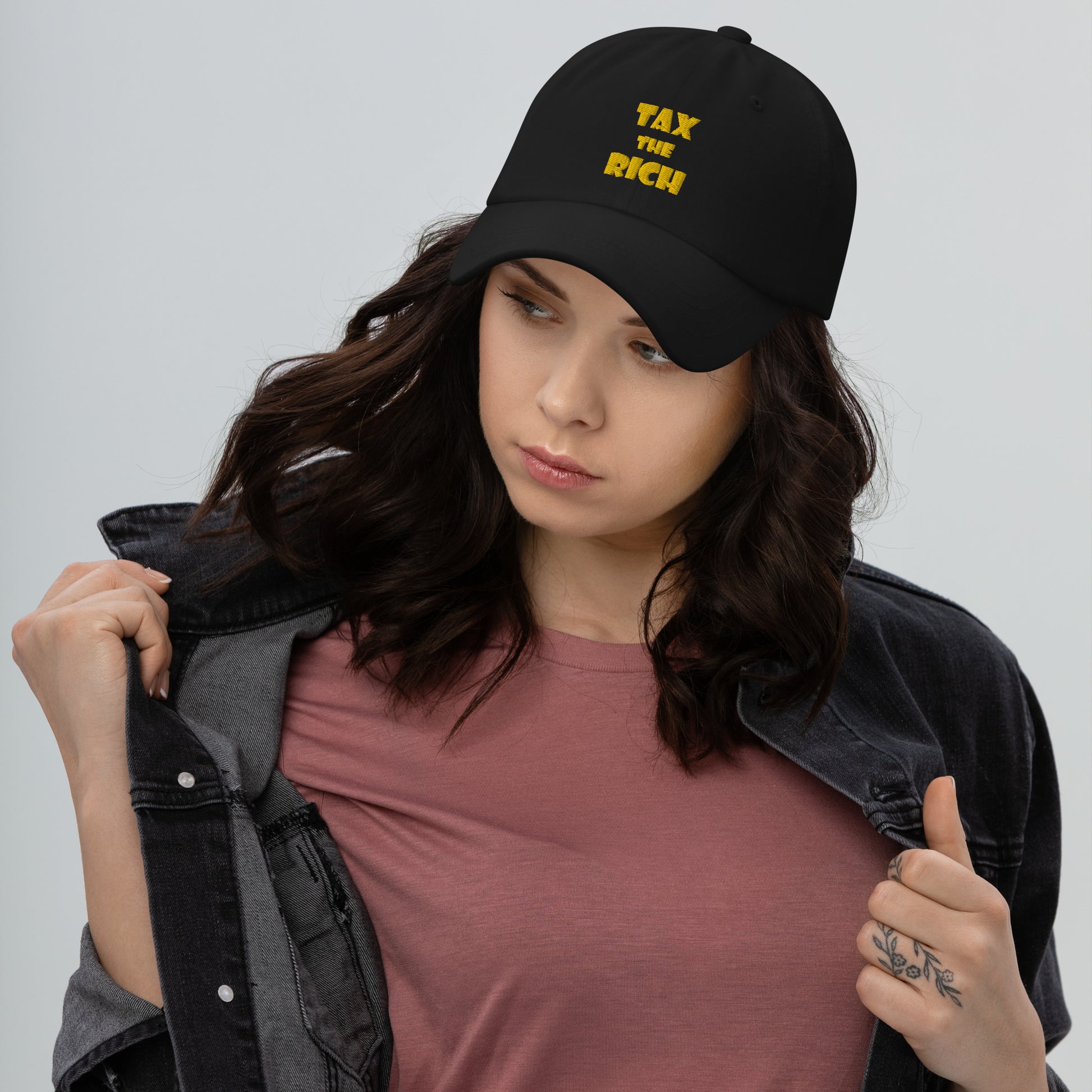 TAX THE RICH — Embroidered Dad Hat worn by a young woman, featuring bold yellow text on a black cap.