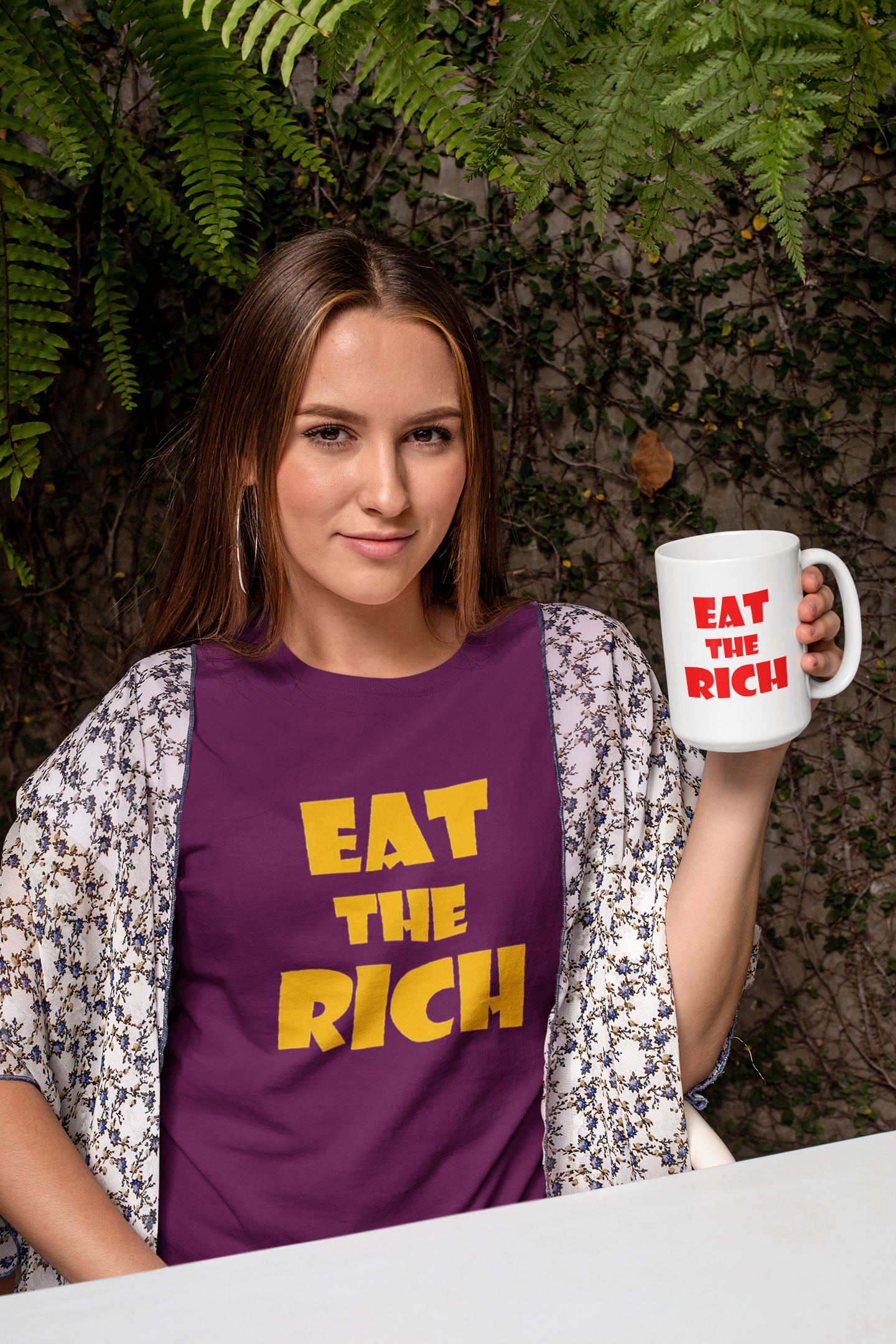 Woman holding a White EAT THE RICH 11oz Ceramic Mug, wearing a purple shirt with bold text.