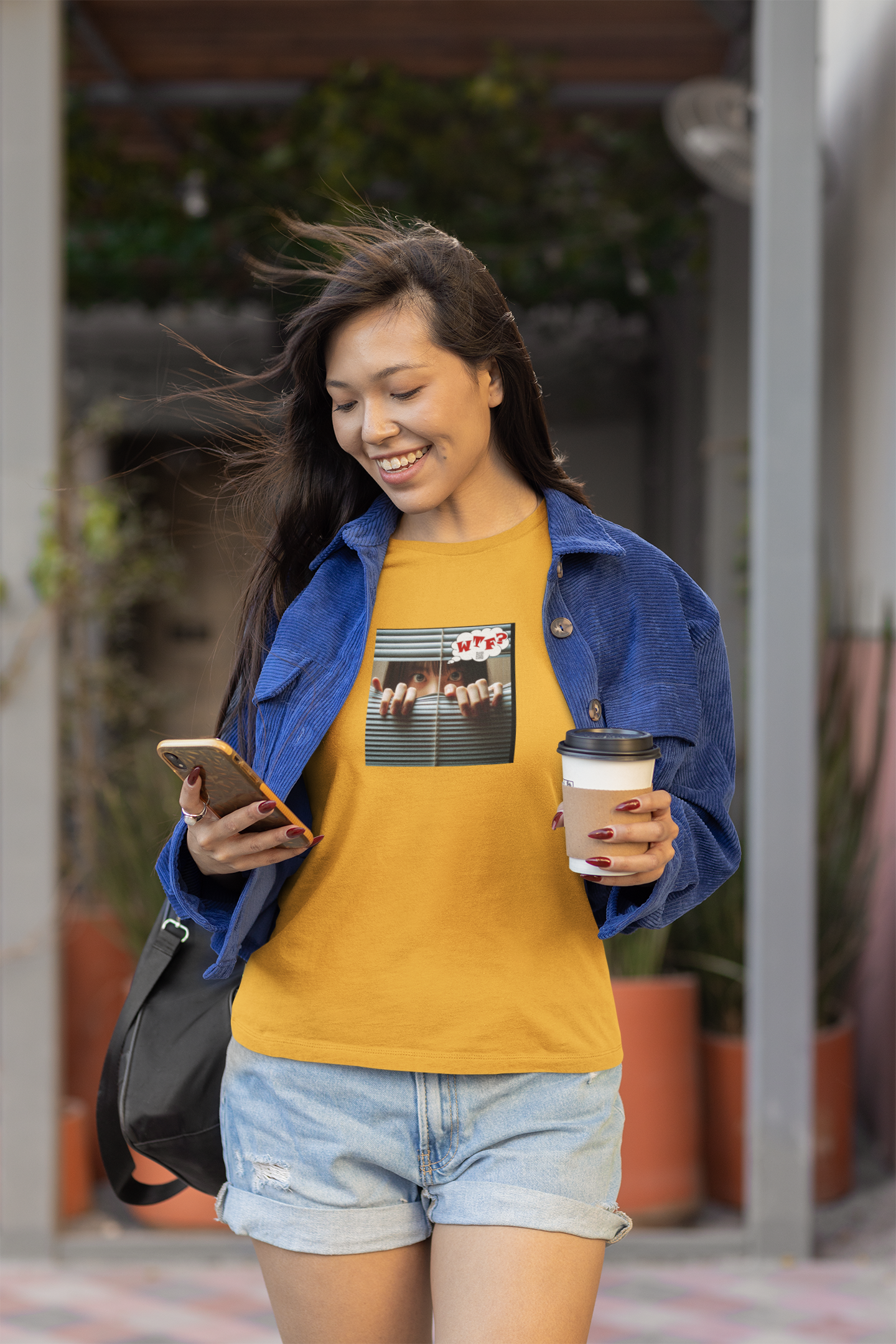 WTF activist t-shirt Asian female model wearing a yellow shirt and blue jacket, smiling while holding coffee and phone.