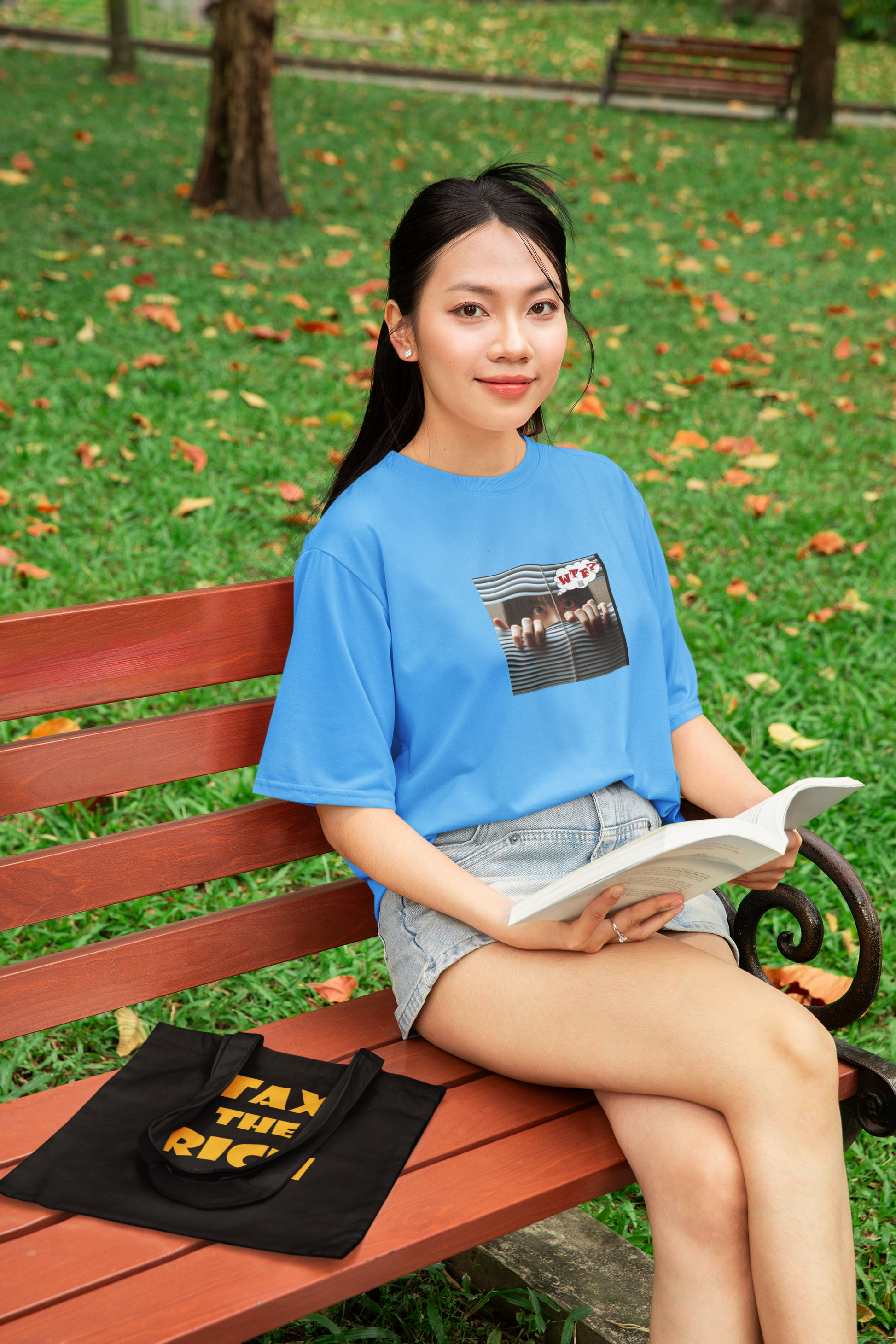 WTF activist t-shirt Asian female model sitting on a bench reading a book in a park.