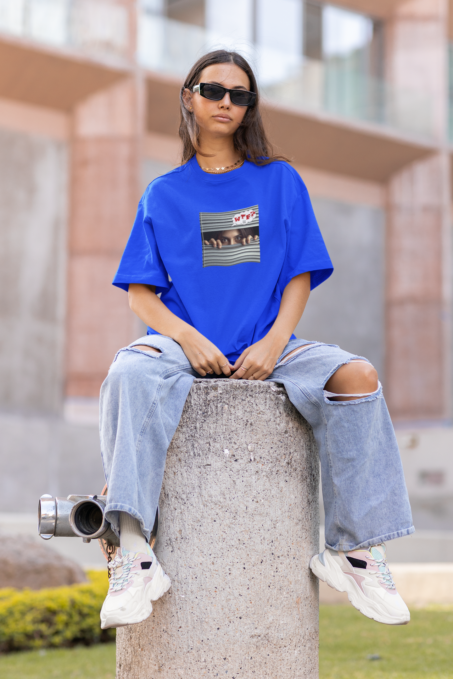 Young Hispanic female activist wearing a blue WTF Hispanic female activist t-shirt, sitting on a concrete pillar.