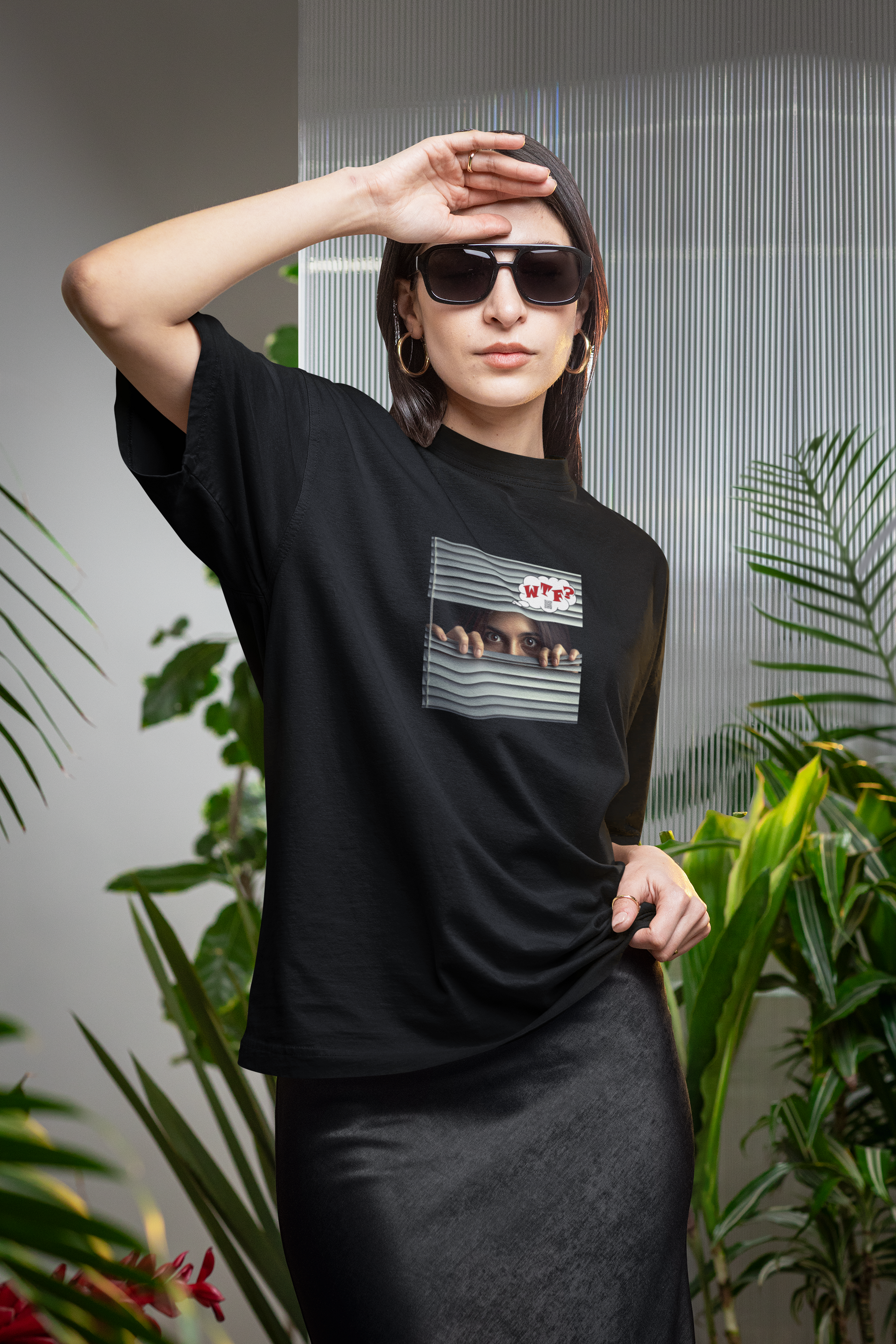 Woman wearing a WTF Hispanic female activist t-shirt in a stylish setting surrounded by plants.