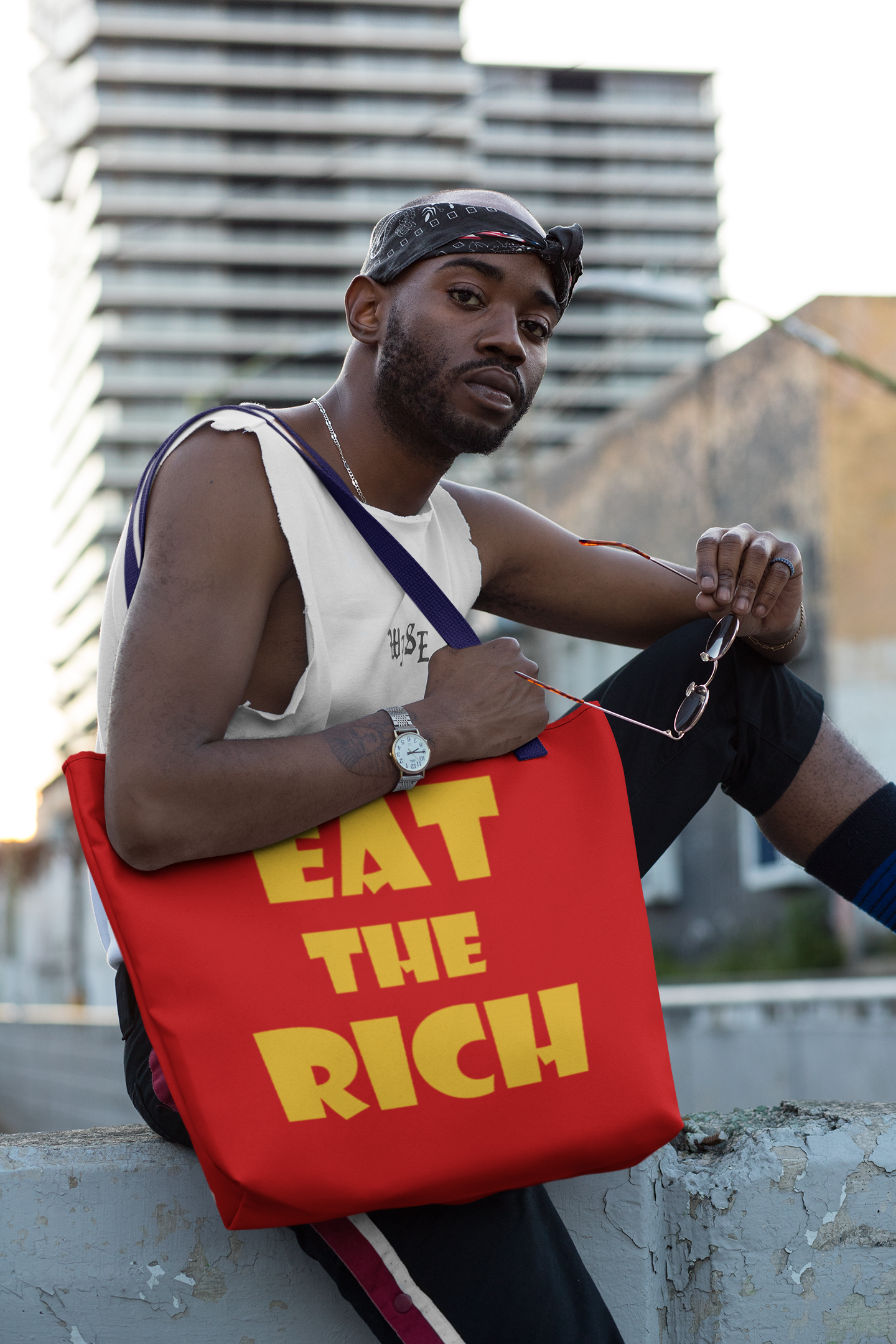 Model holding the Eat the Rich accessory tote bag with bold typography in an urban setting.