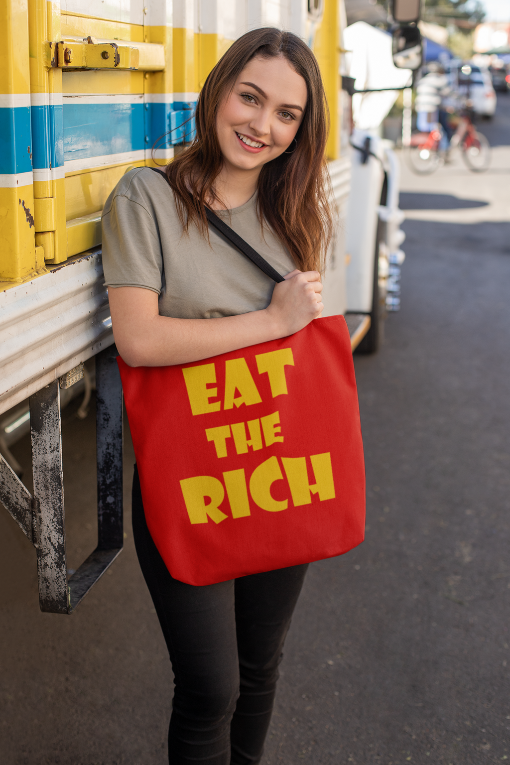 A person holding an Eat the Rich accessory tote bag featuring bold typography, promoting a message of wealth critique.
