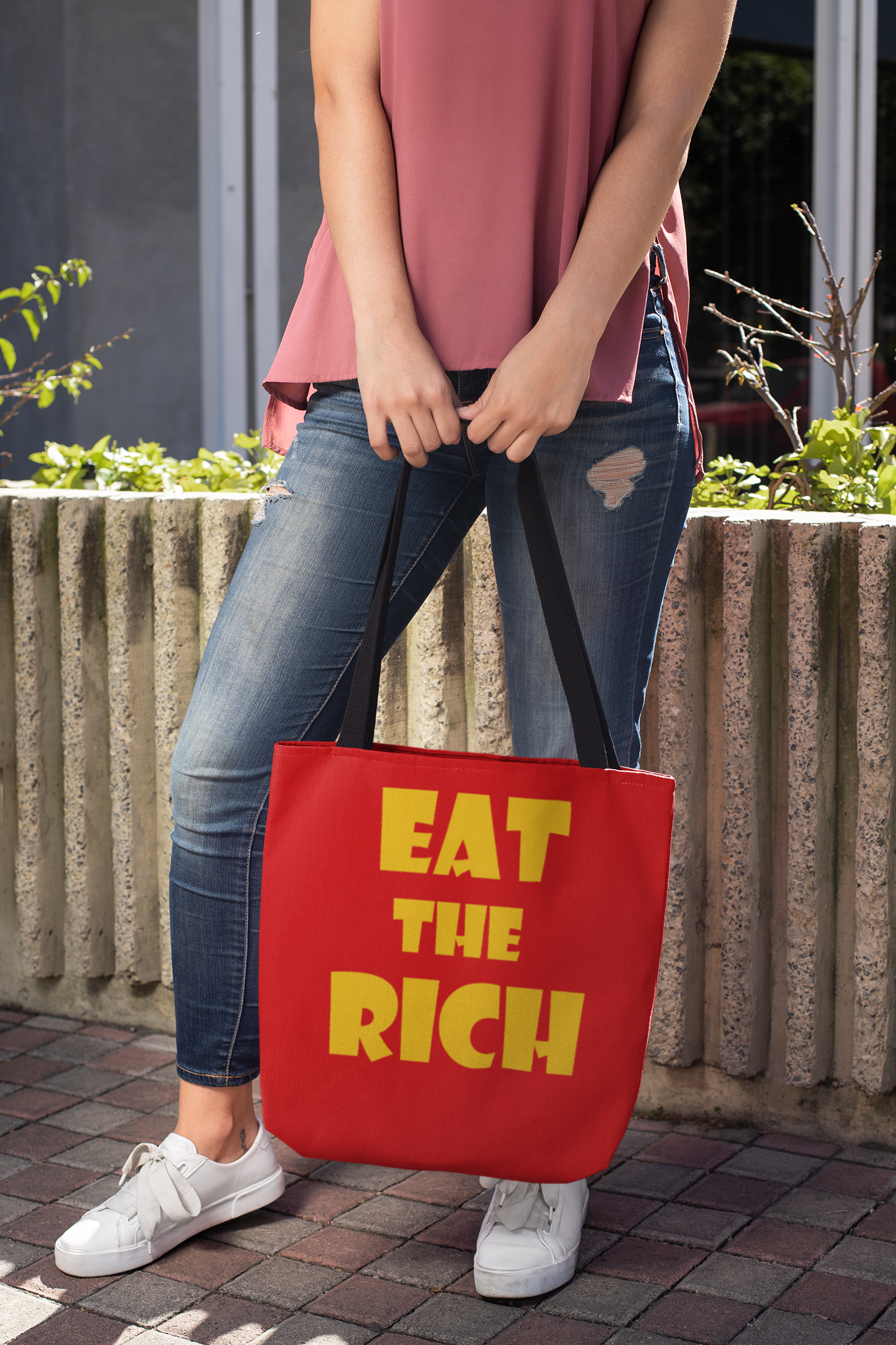 Person holding an Eat the Rich accessory tote bag with bold typography in a casual outdoor setting.