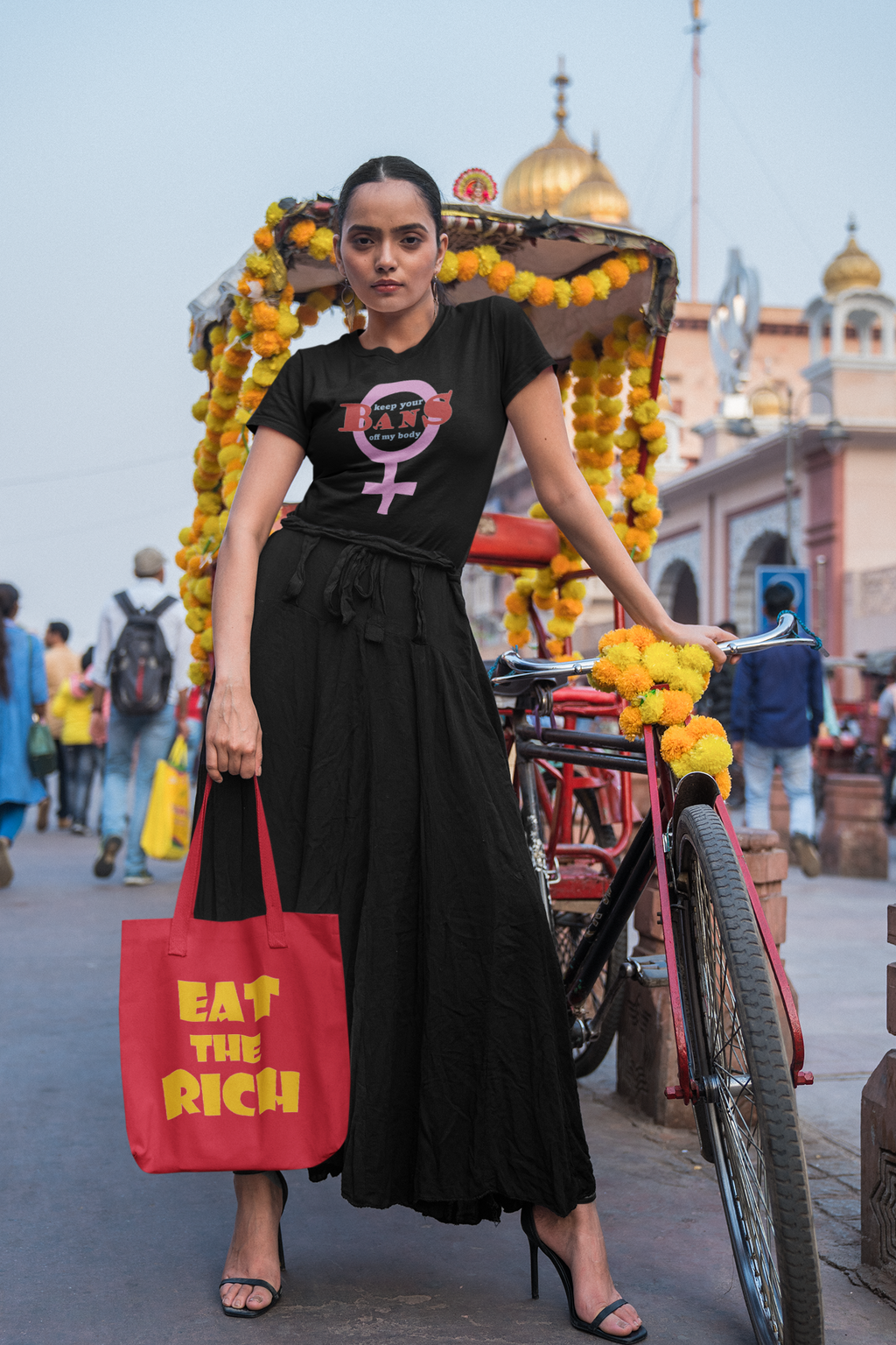 Model poses with an Eat the Rich accessory tote bag, showcasing bold design against a busy street backdrop.