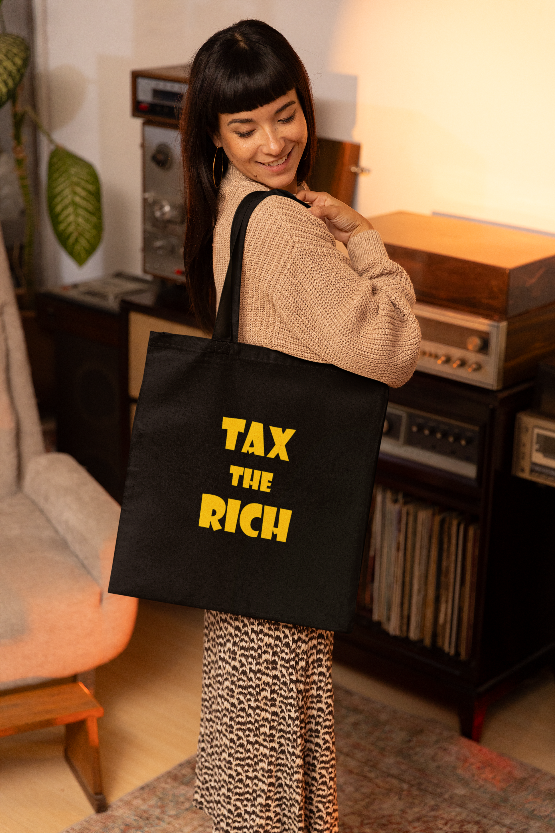 Woman carrying a black tote bag with bold text reading 'TAX THE RICH', showcasing the Tax the Rich accessory tote bag.