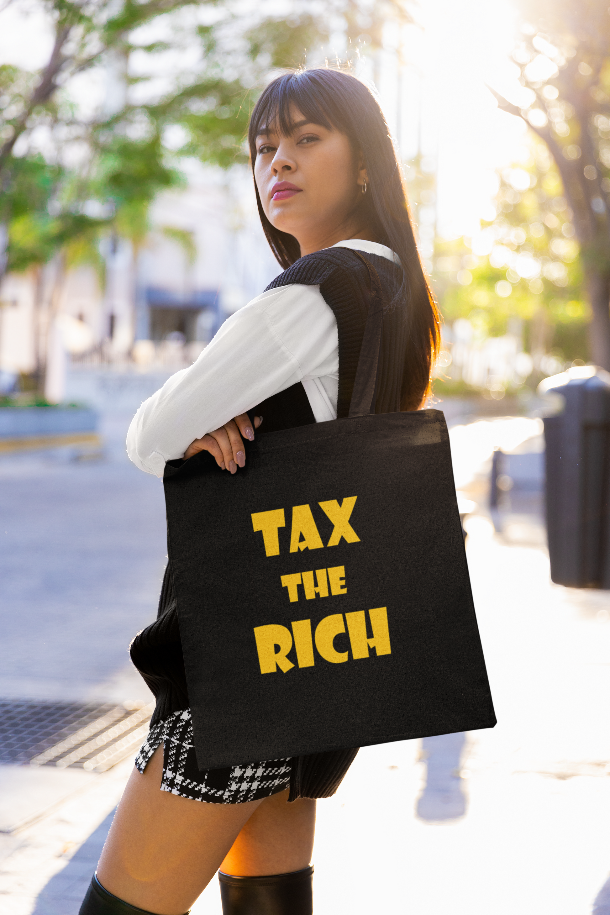 Model holding a black tote bag with the phrase 'TAX THE RICH' in bold letters, showcasing the Tax the Rich accessory tote bag.