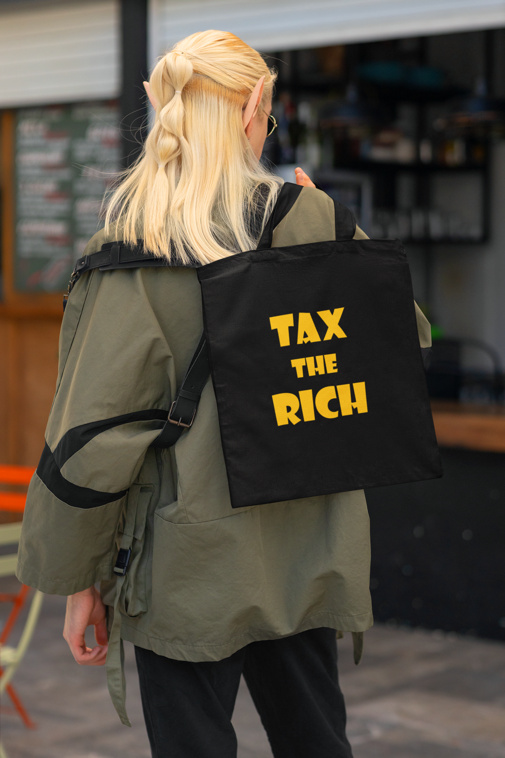 Person wearing Tax the Rich accessory tote bag with bold text design, highlighting wealth inequality.