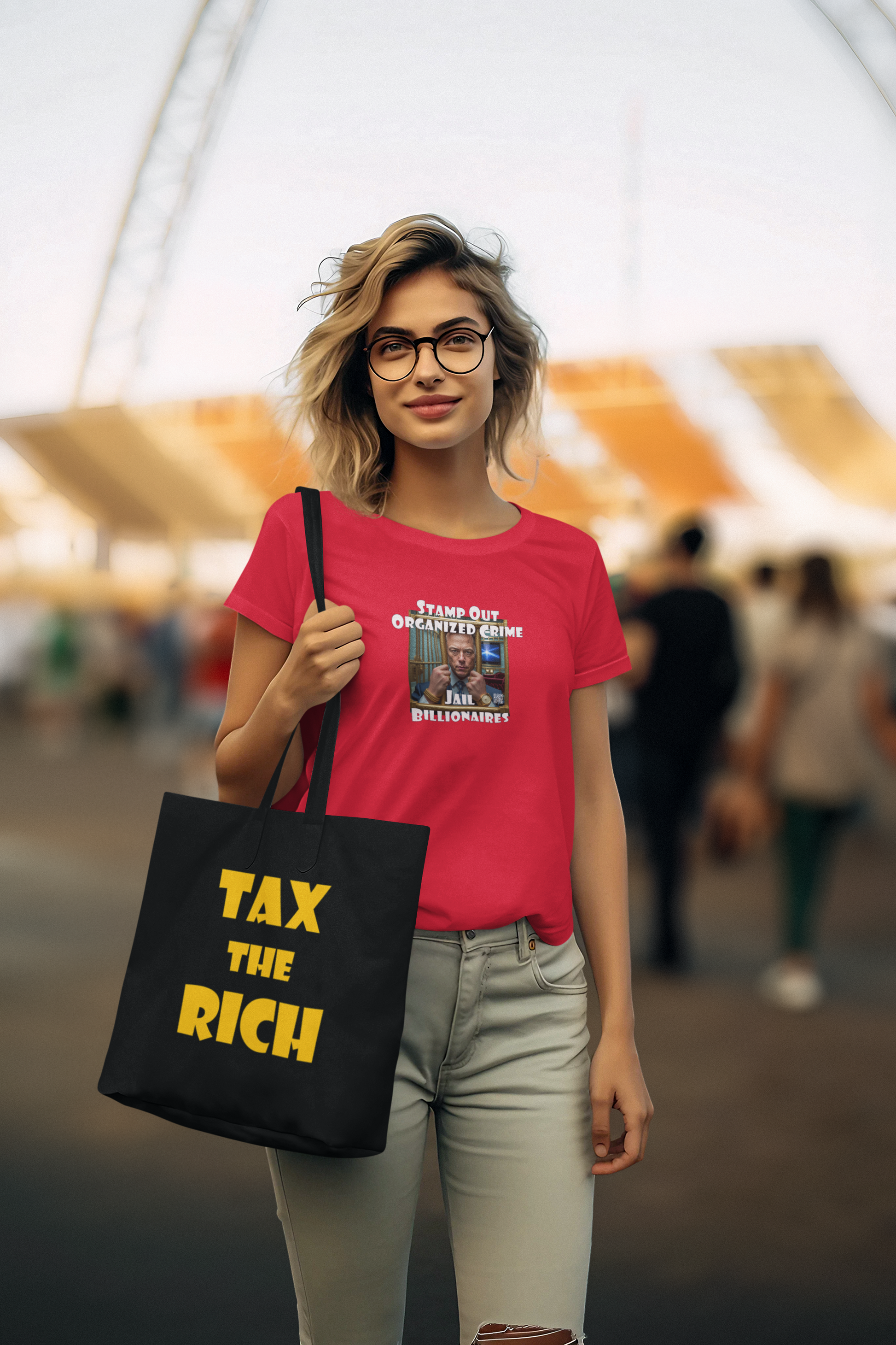 Model wearing a red shirt and holding a Tax the Rich accessory tote bag in a crowded outdoor setting.