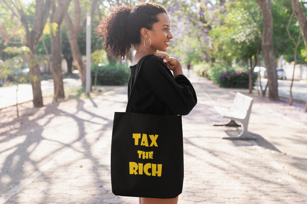 Woman carrying a tote bag with "TAX THE RICH" design, promoting wealth inequality awareness.