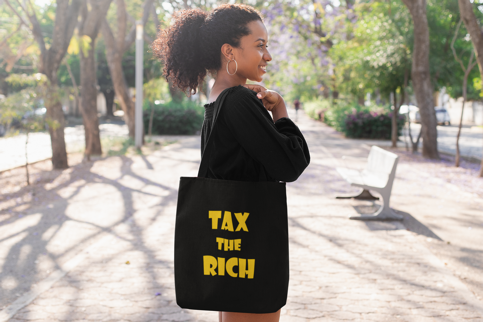 Woman carrying a tote bag with "TAX THE RICH" design, promoting wealth inequality awareness.