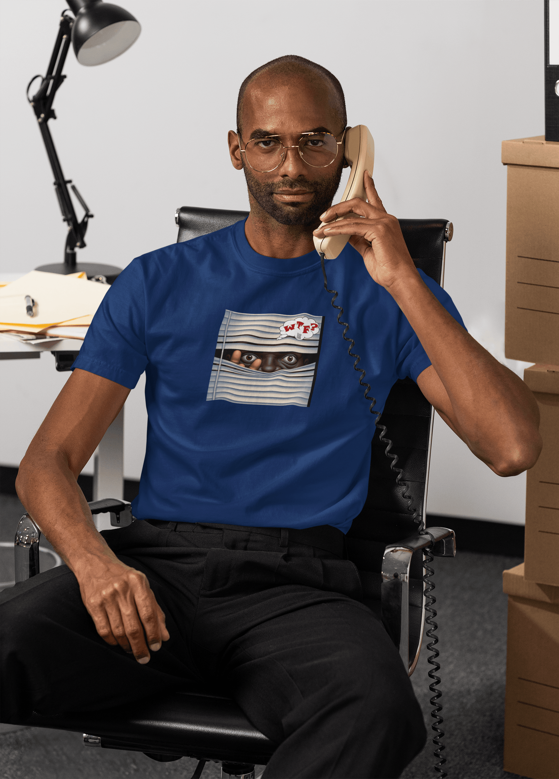 Middle aged black male activist answering phones in an office wearing wire rimmed glasses and a navy unisex WTF? tshirt featuring a black man peering through venetian blinds saying WTF?
