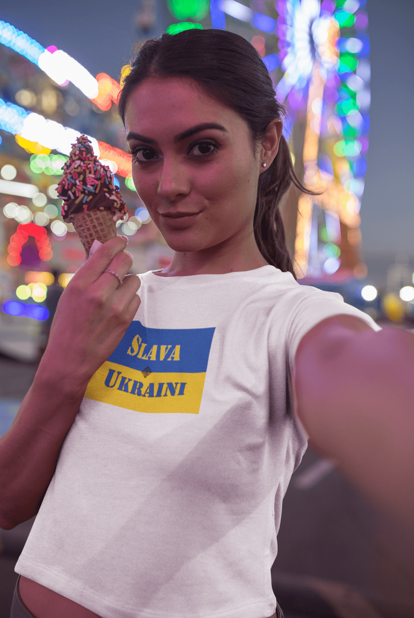 A woman wearing a Slava Ukraini Tee Shirt holding an ice cream cone in a vibrant, festive setting.