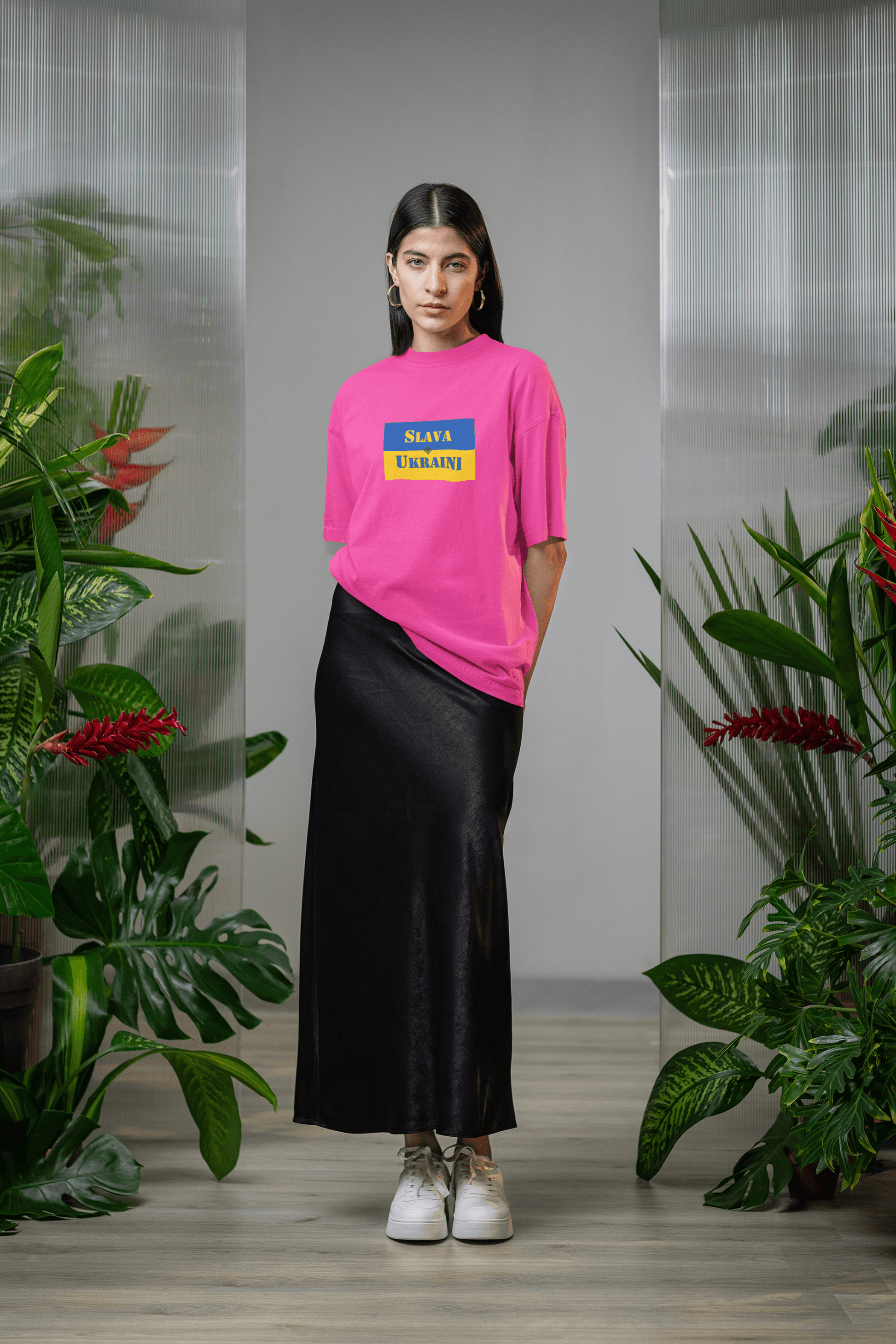 Model wearing Slava Ukraini Tee Shirt in pink with black skirt, surrounded by greenery.