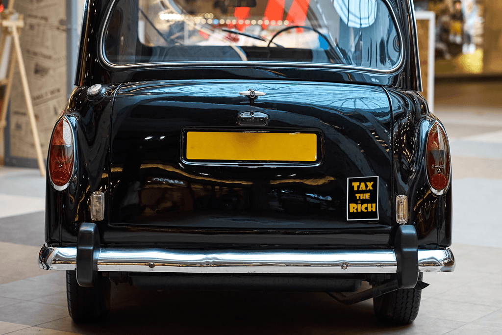 4" x 5" black vinyl magnet with Tax the Rich in gold lettering stuck to the back of a black UK taxi cab