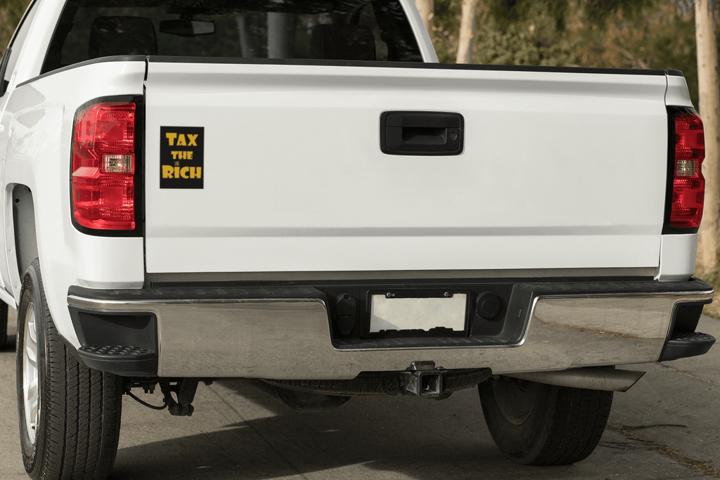 4" x 5" black vinyl magnet with Tax the Rich in gold lettering stuck to the back of a white pickup truck near the left tail light