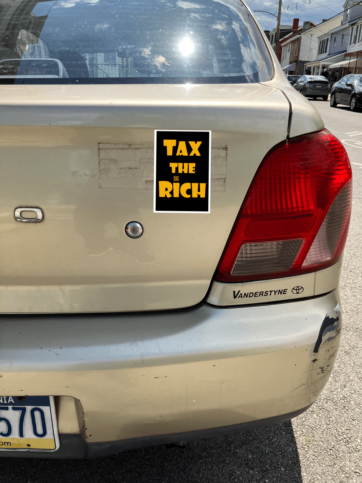 4" x 5" black vinyl magnet with Tax the Rich in gold lettering stuck to the back of a gold car