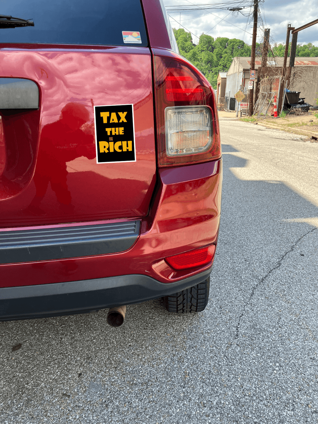 4" x 5" black vinyl magnet with Tax the Rich in gold lettering stuck to the back of a red car