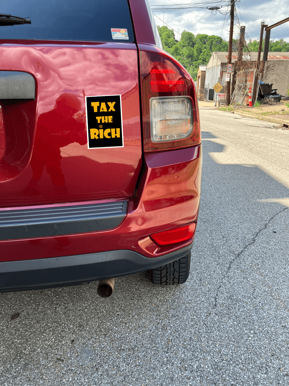 4" x 5" black vinyl magnet with Tax the Rich in gold lettering stuck to the back of a red car