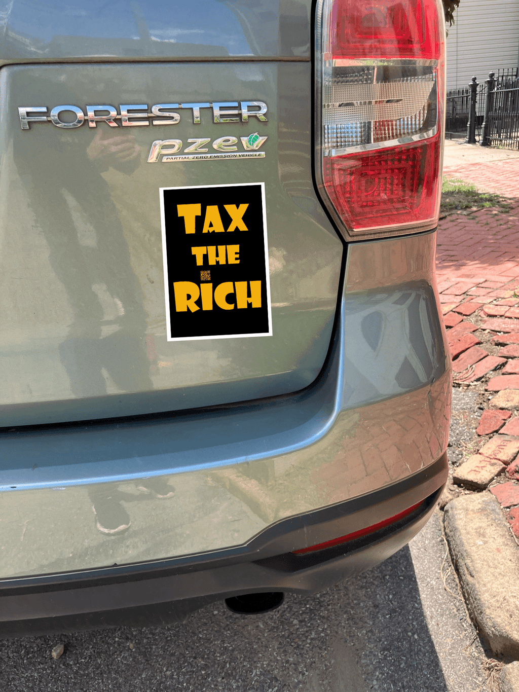 4" x 5" black vinyl magnet with Tax the Rich in gold lettering stuck to the back of a green car